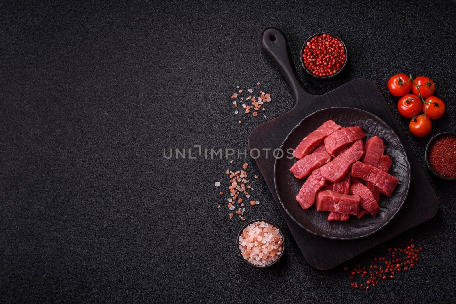 Raw beef tenderloin cut into slices with salt and spices on a dark concrete background
