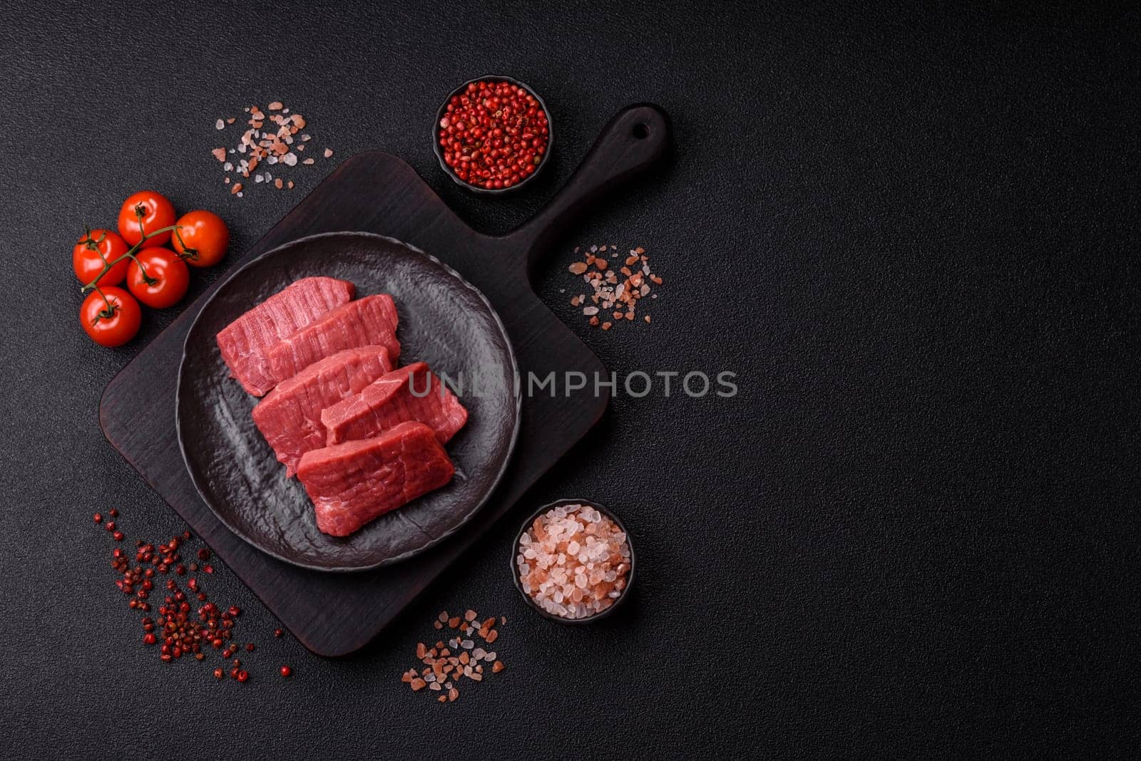 Raw beef tenderloin cut into slices with salt and spices on a dark concrete background
