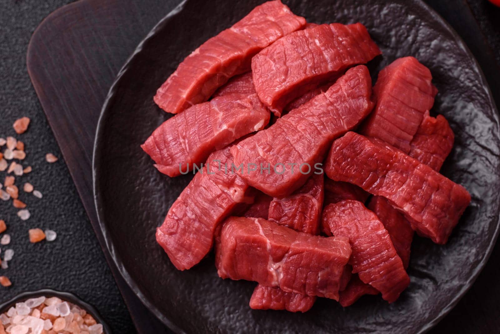 Raw beef tenderloin cut into slices with salt and spices on a dark concrete background