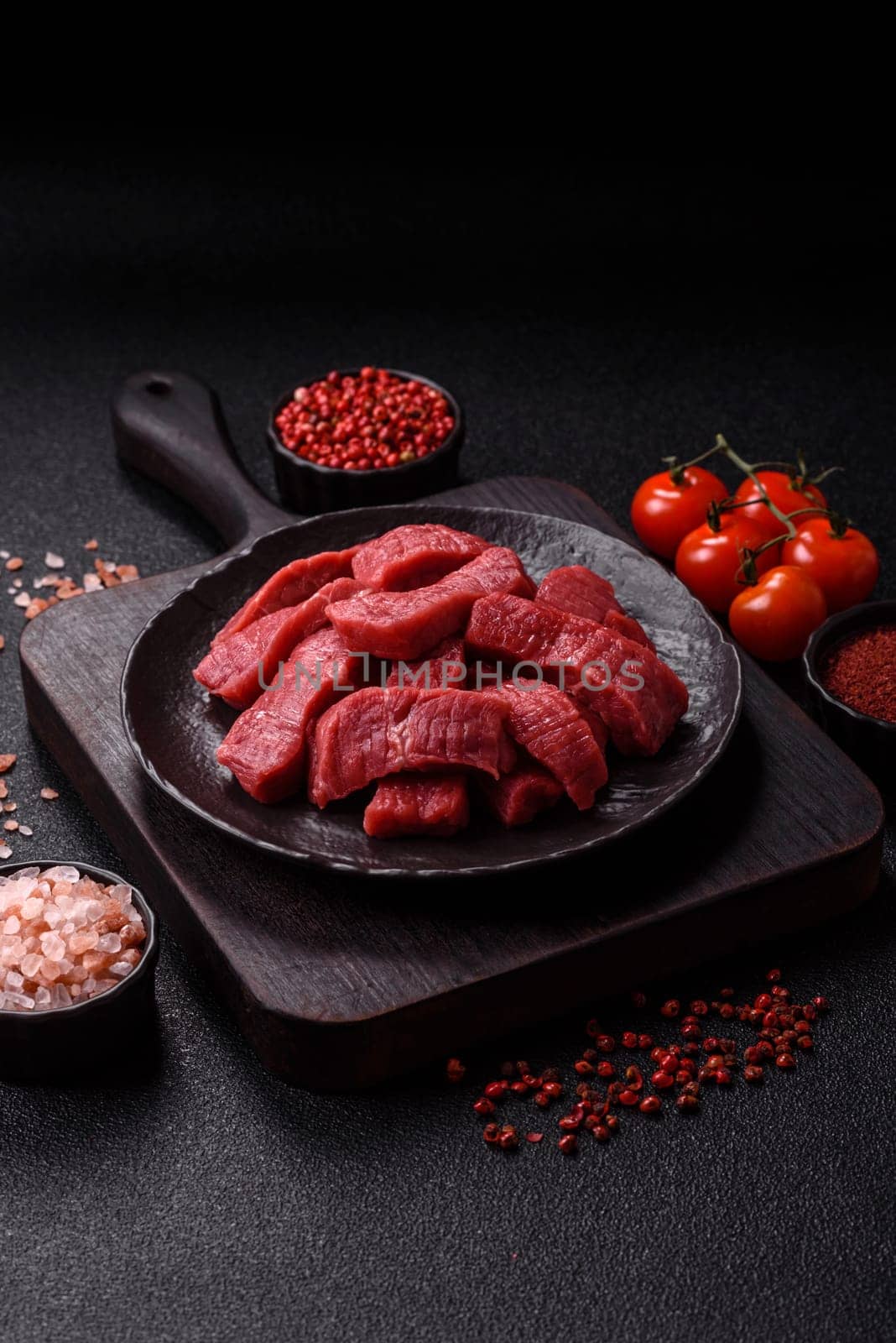Raw beef tenderloin cut into slices with salt and spices on a dark concrete background