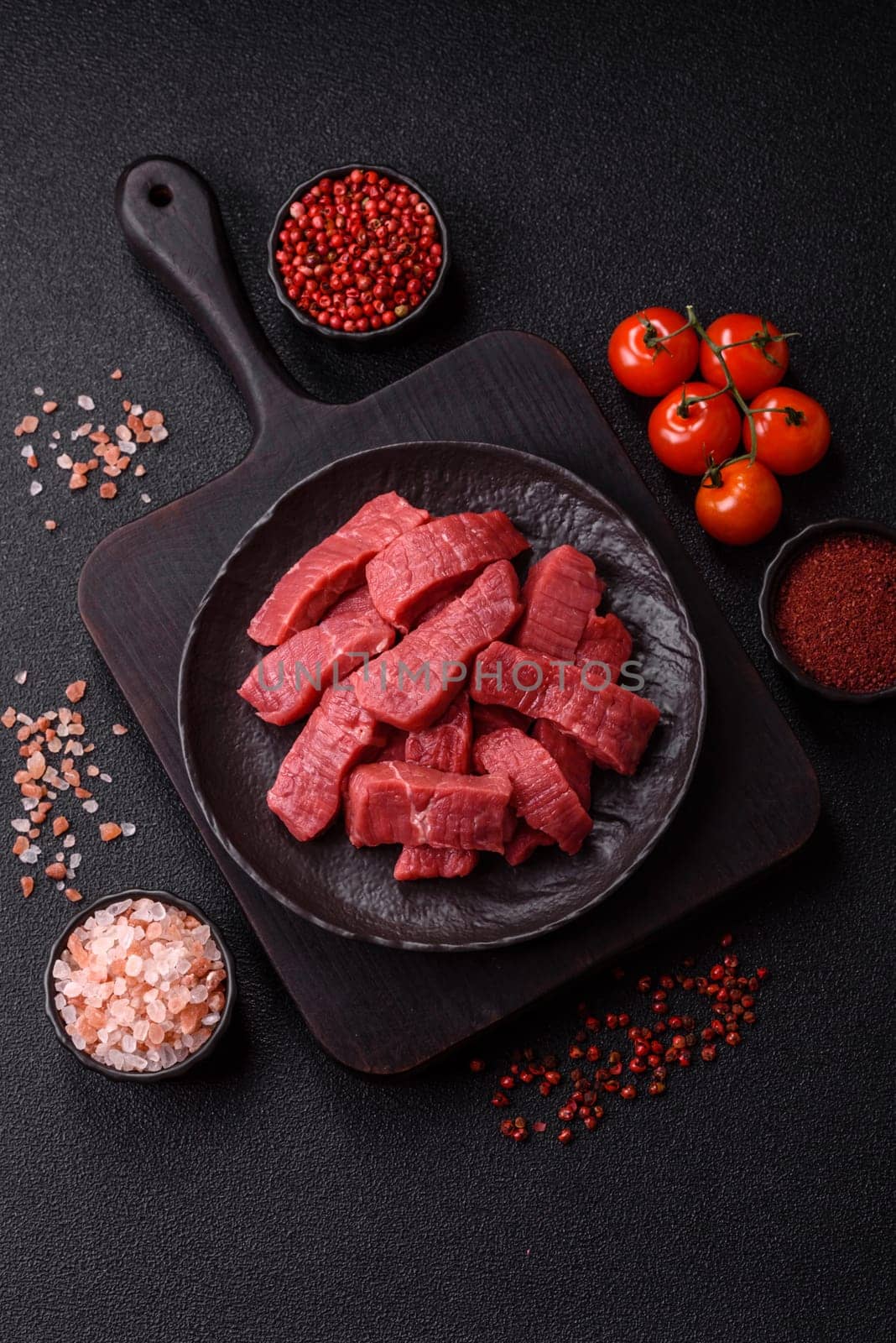 Raw beef tenderloin cut into slices with salt and spices on a dark concrete background