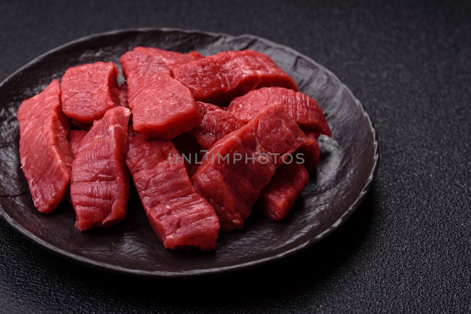 Raw beef tenderloin cut into slices with salt and spices on a dark concrete background