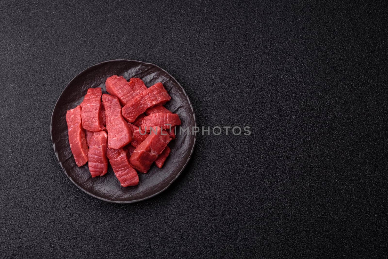Raw beef tenderloin cut into slices with salt and spices on a dark concrete background