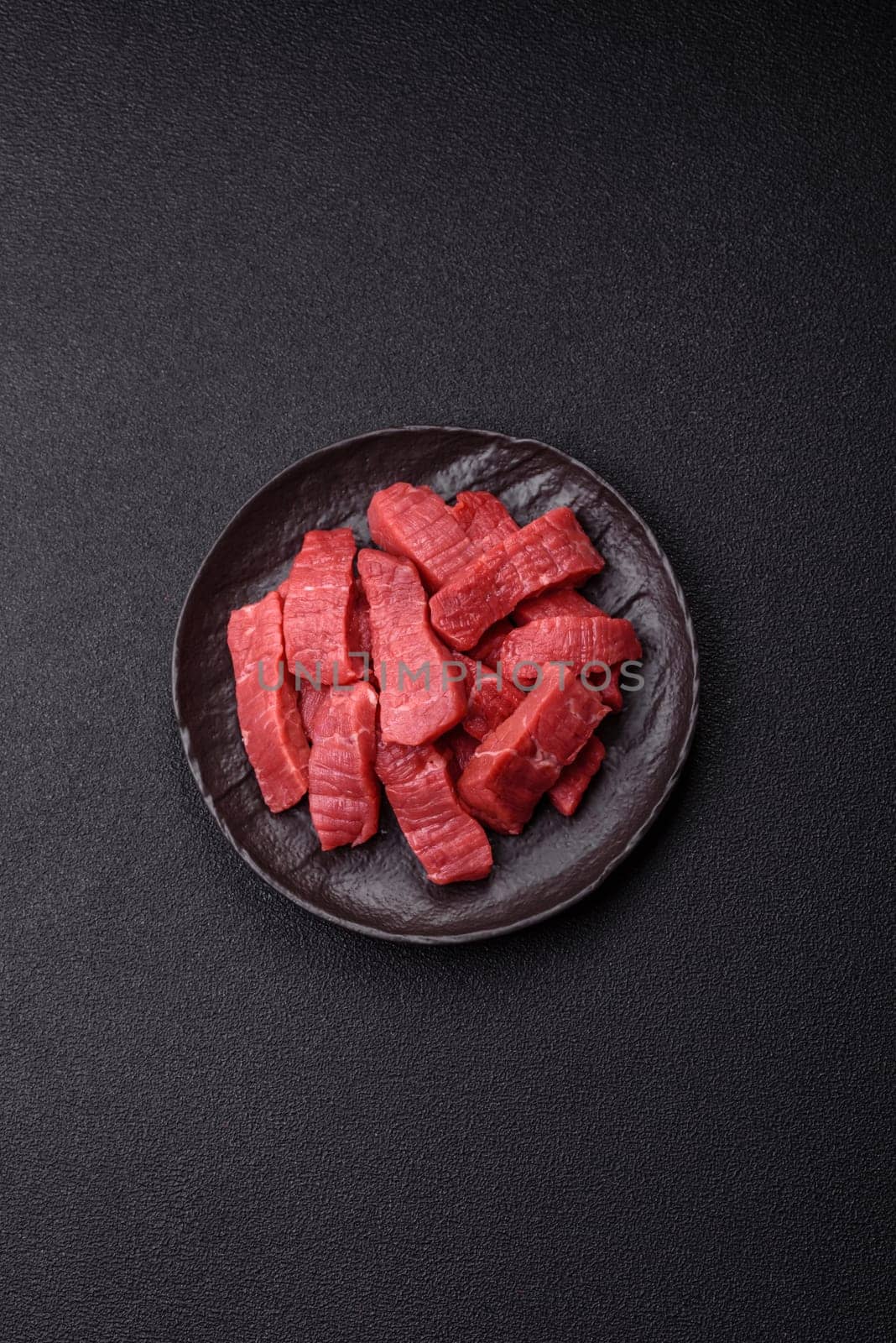 Raw beef tenderloin cut into slices with salt and spices on a dark concrete background