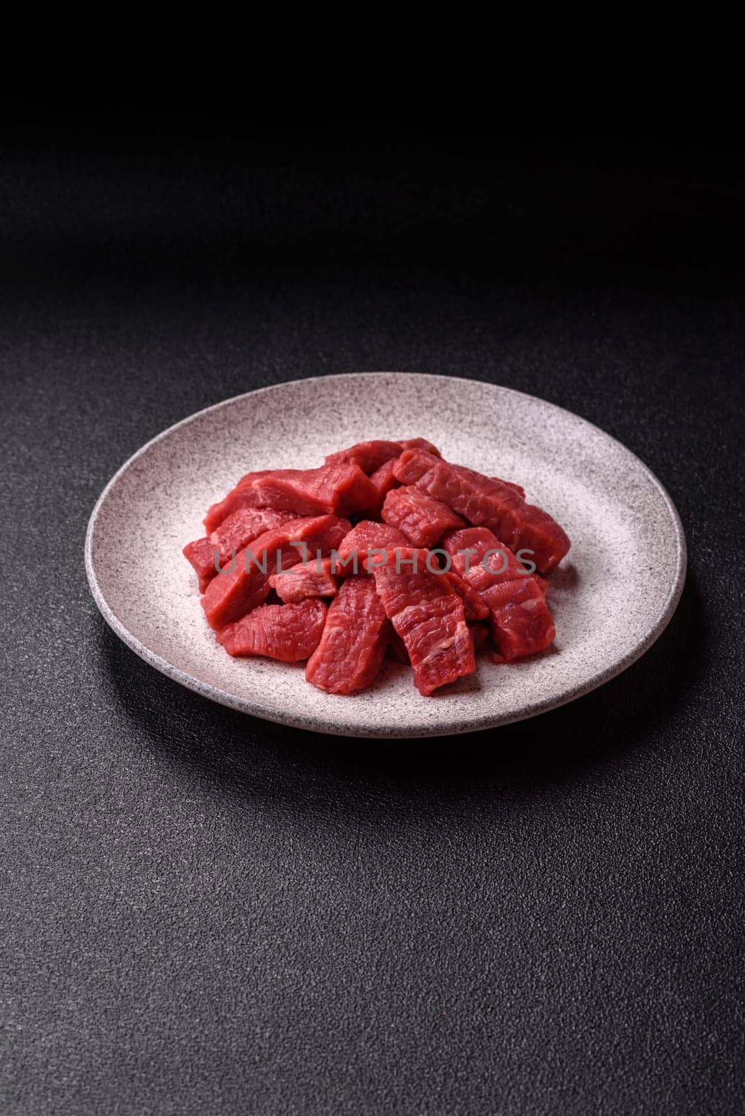 Raw beef tenderloin cut into slices with salt and spices on a dark concrete background