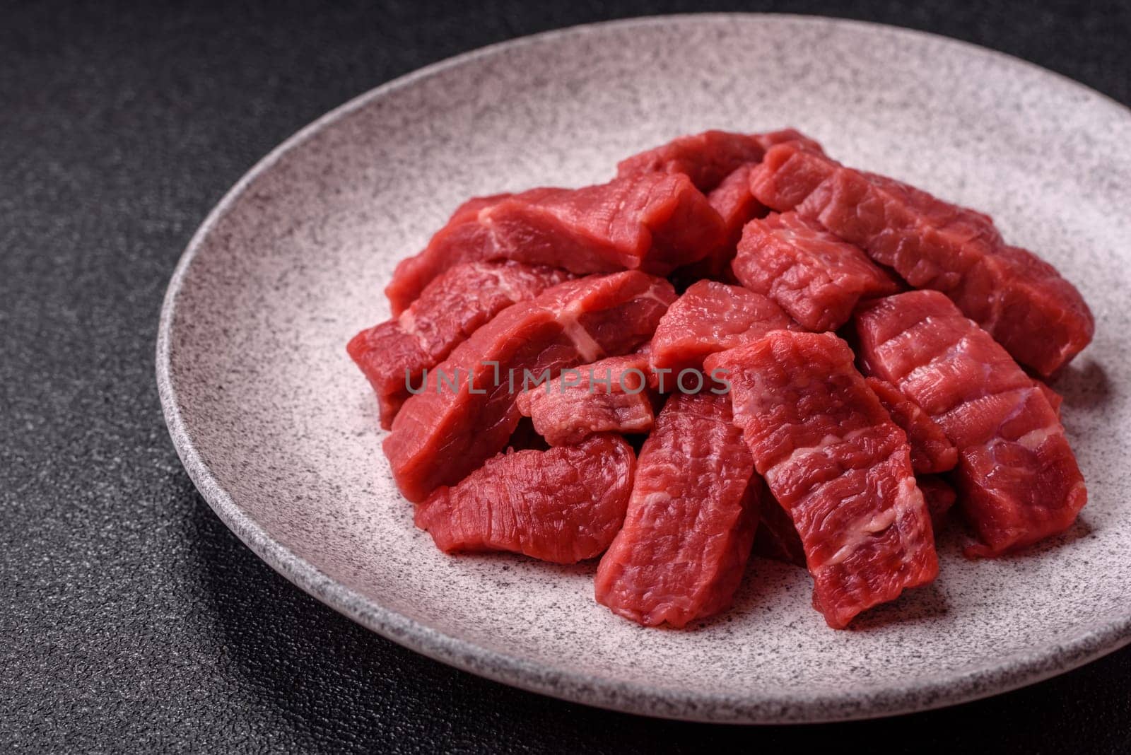 Raw beef tenderloin cut into slices with salt and spices on a dark concrete background