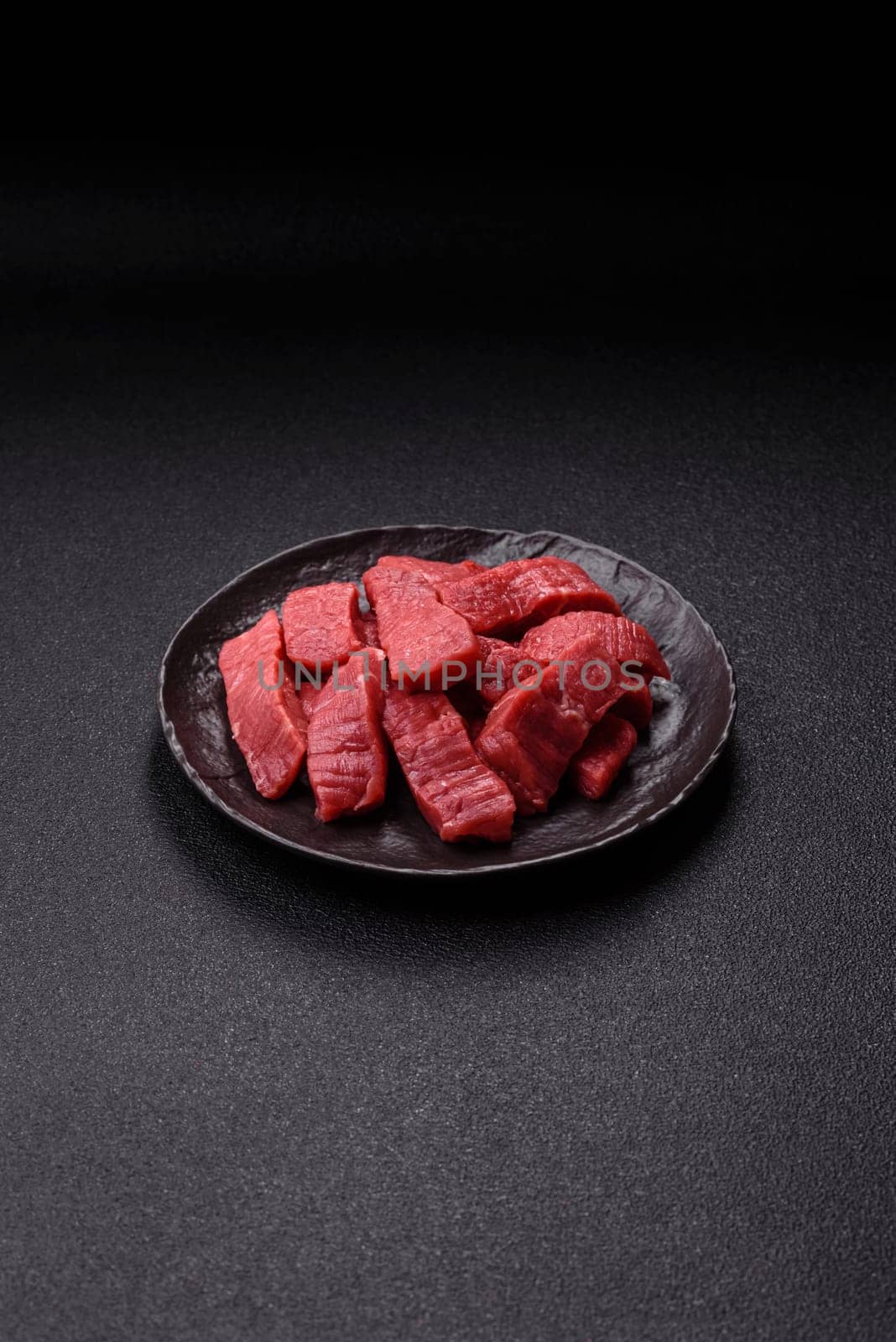 Raw beef tenderloin cut into slices with salt and spices on a dark concrete background