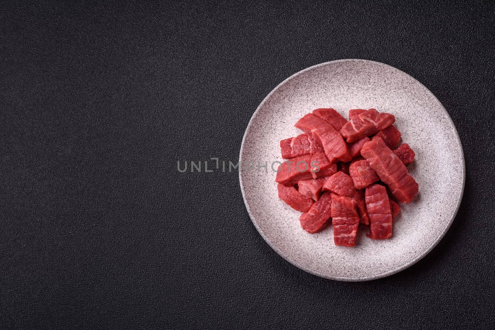 Raw beef tenderloin cut into slices with salt and spices on a dark concrete background