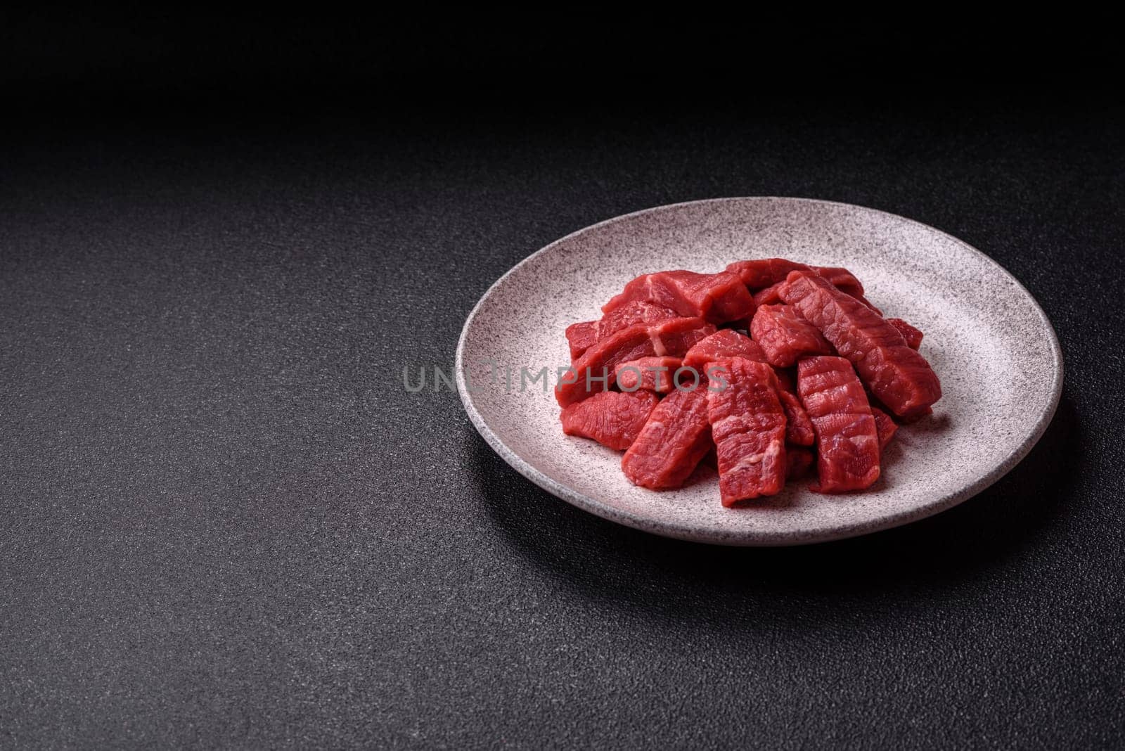 Raw beef tenderloin cut into slices with salt and spices on a dark concrete background