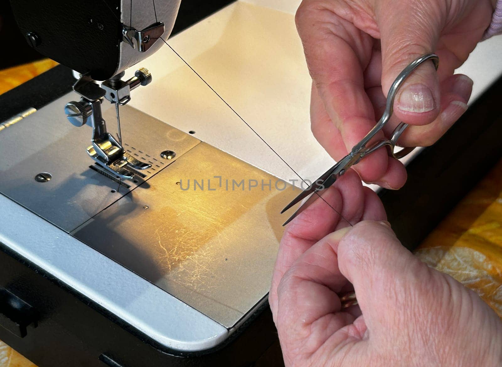 Close-up of hands using scissors to cut thread on a sewing machine, demonstrating precision and skill in tailoring.