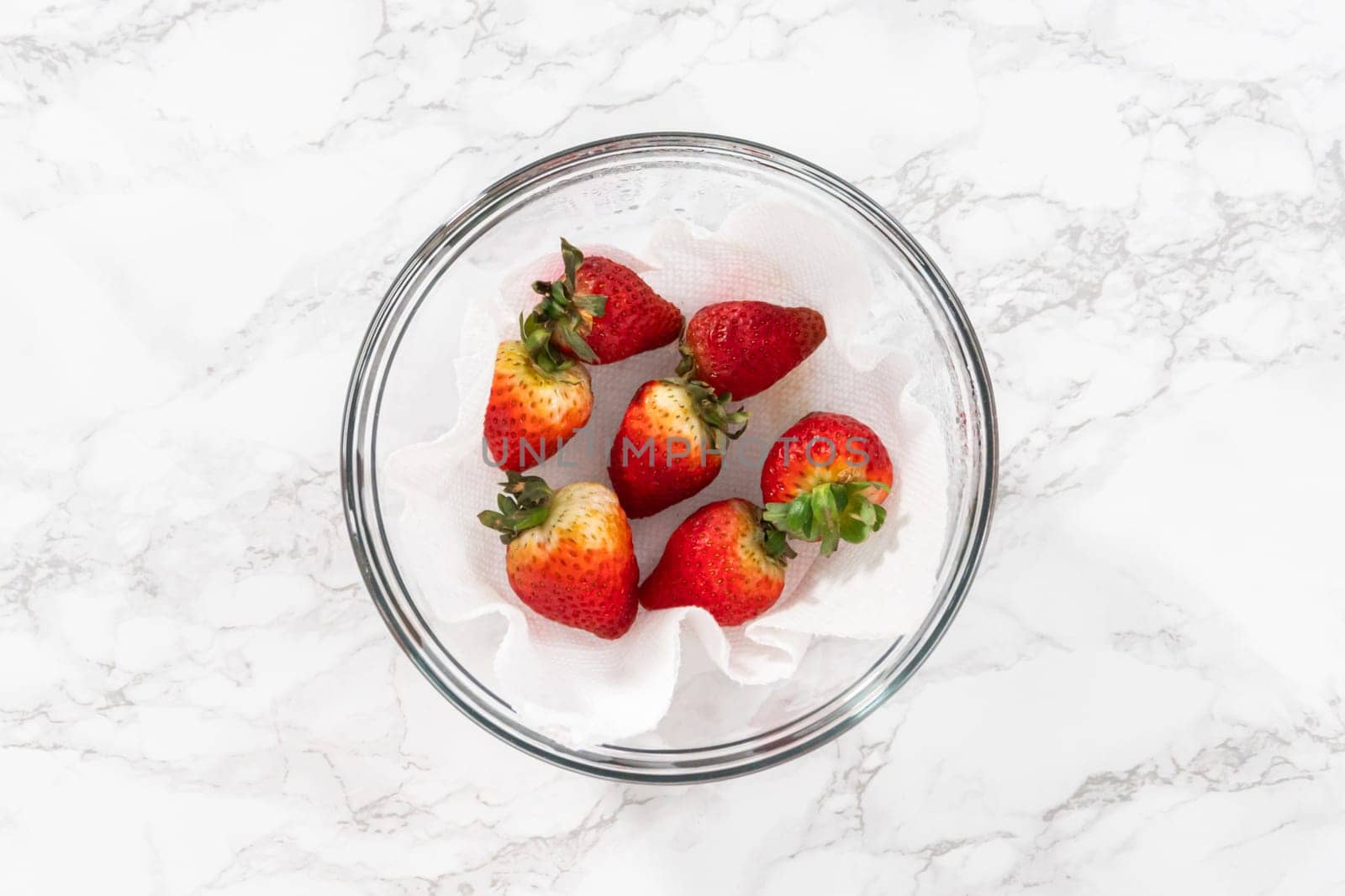 Freshly washed and dried strawberries are carefully arranged in a glass bowl lined with paper towel, ready for snacking or further use.