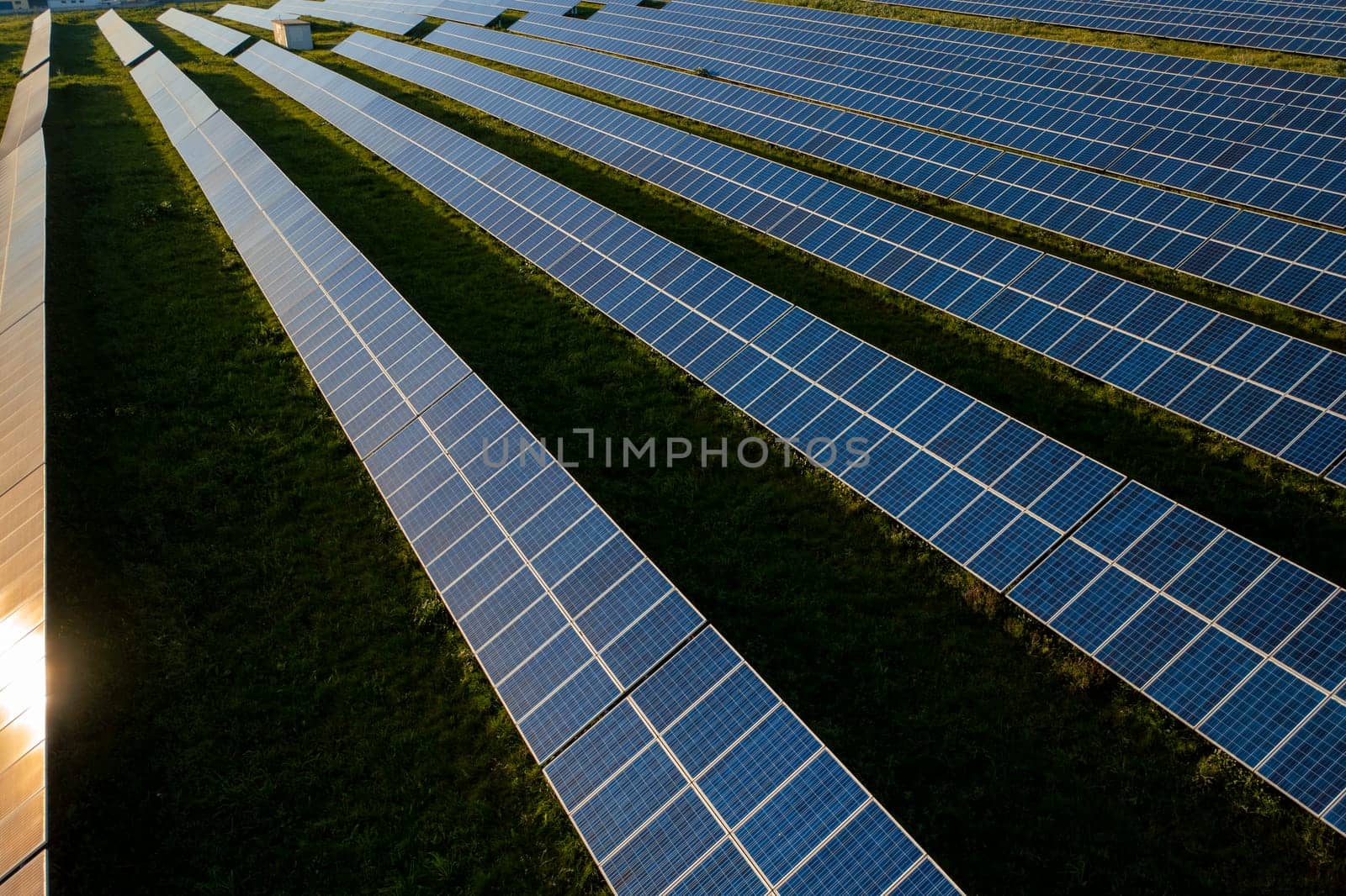 Drone view of blue solar panels on agricultural field during sunny day. The landscape is fully equipped with green renewable energy generators