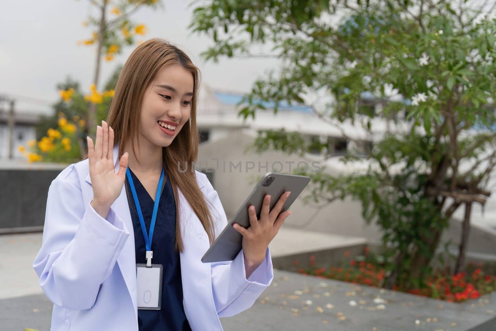 A cheerful young female physician waves while on a video call outside, representing modern communication in healthcare.