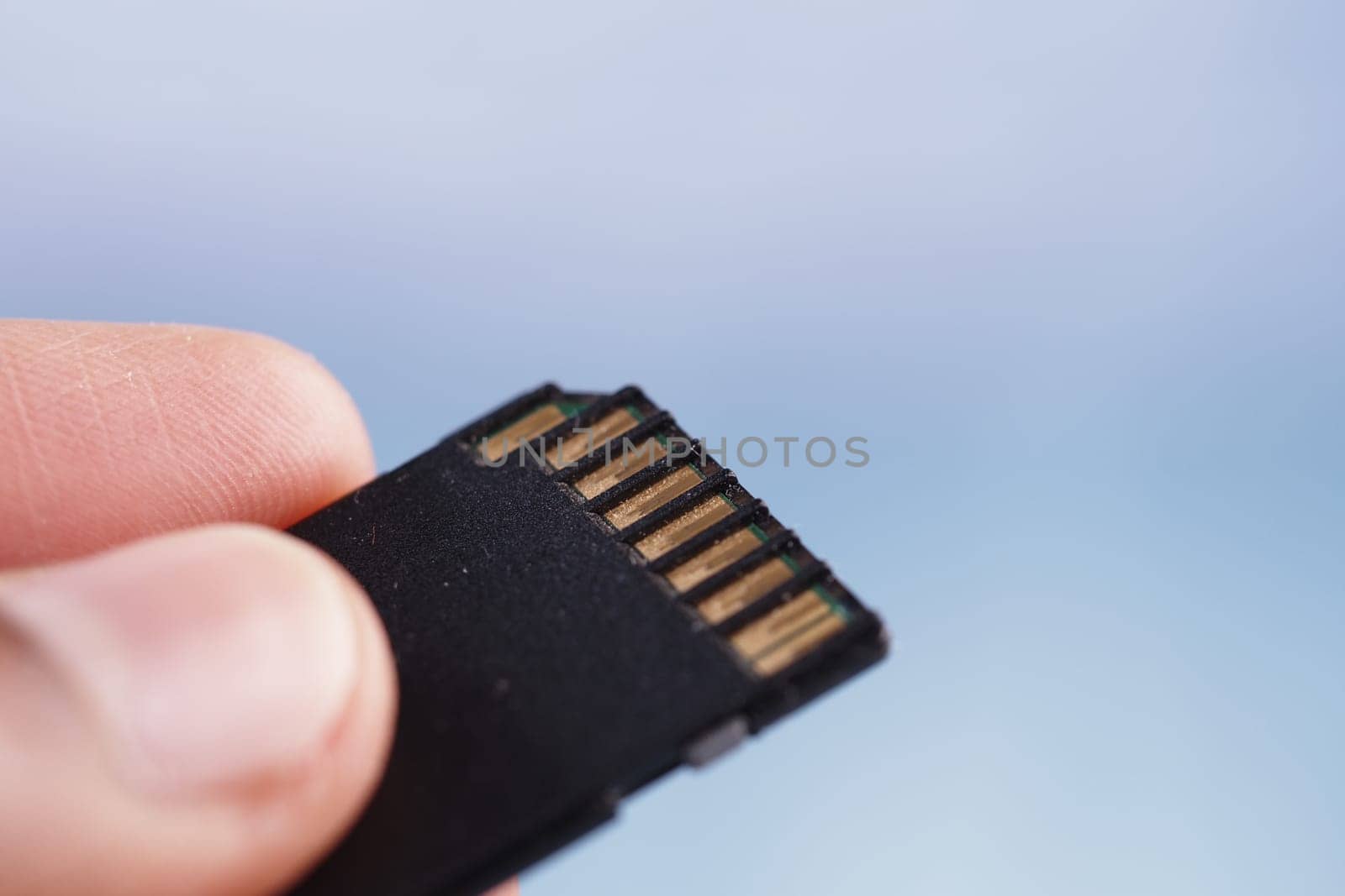 A person holds a micro SD card, showcasing its metallic connectors clearly.