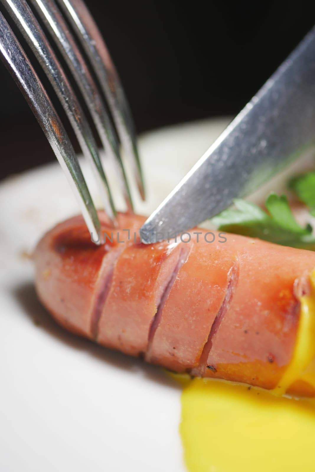 Sliced sausage on a plate with sauce and fresh greens, being cut.
