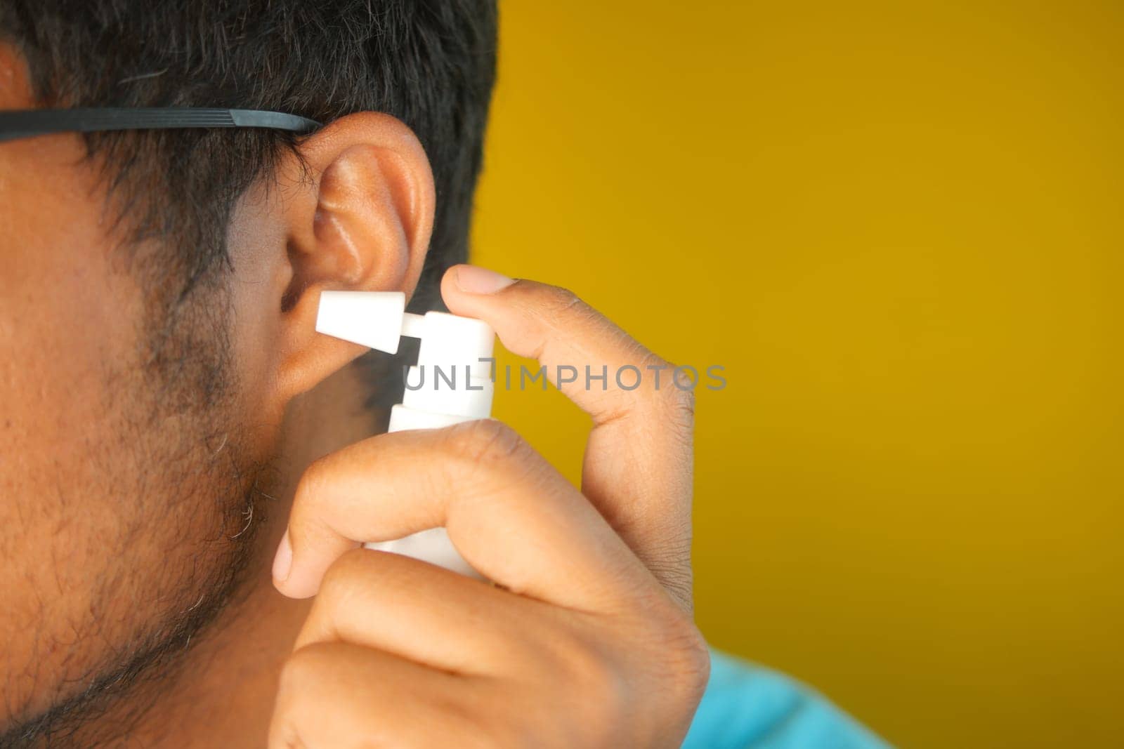 A man is using ear spray for personal hygiene in a bright setting.