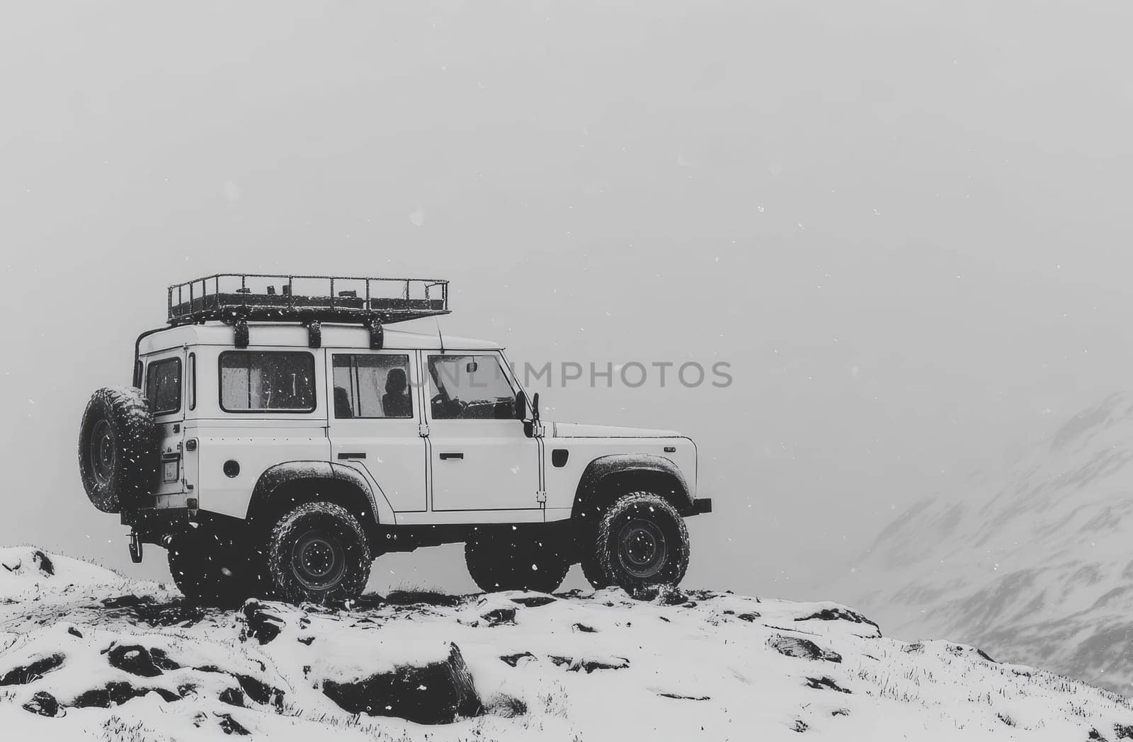 A white all-terrain vehicle is parked on a snowy mountain peak in the midst of a snowstorm. The vehicle's robust design contrasts with the soft, snowy landscape. A mountain range rises in background.