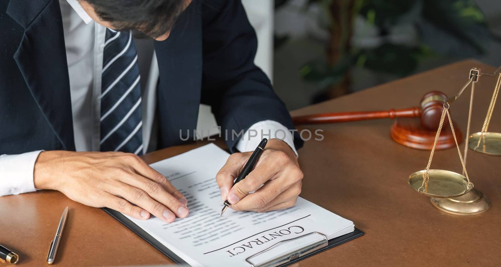 A lawyer is diligently reviewing and signing contract documents, with a gavel and scales of justice visible on the desk.