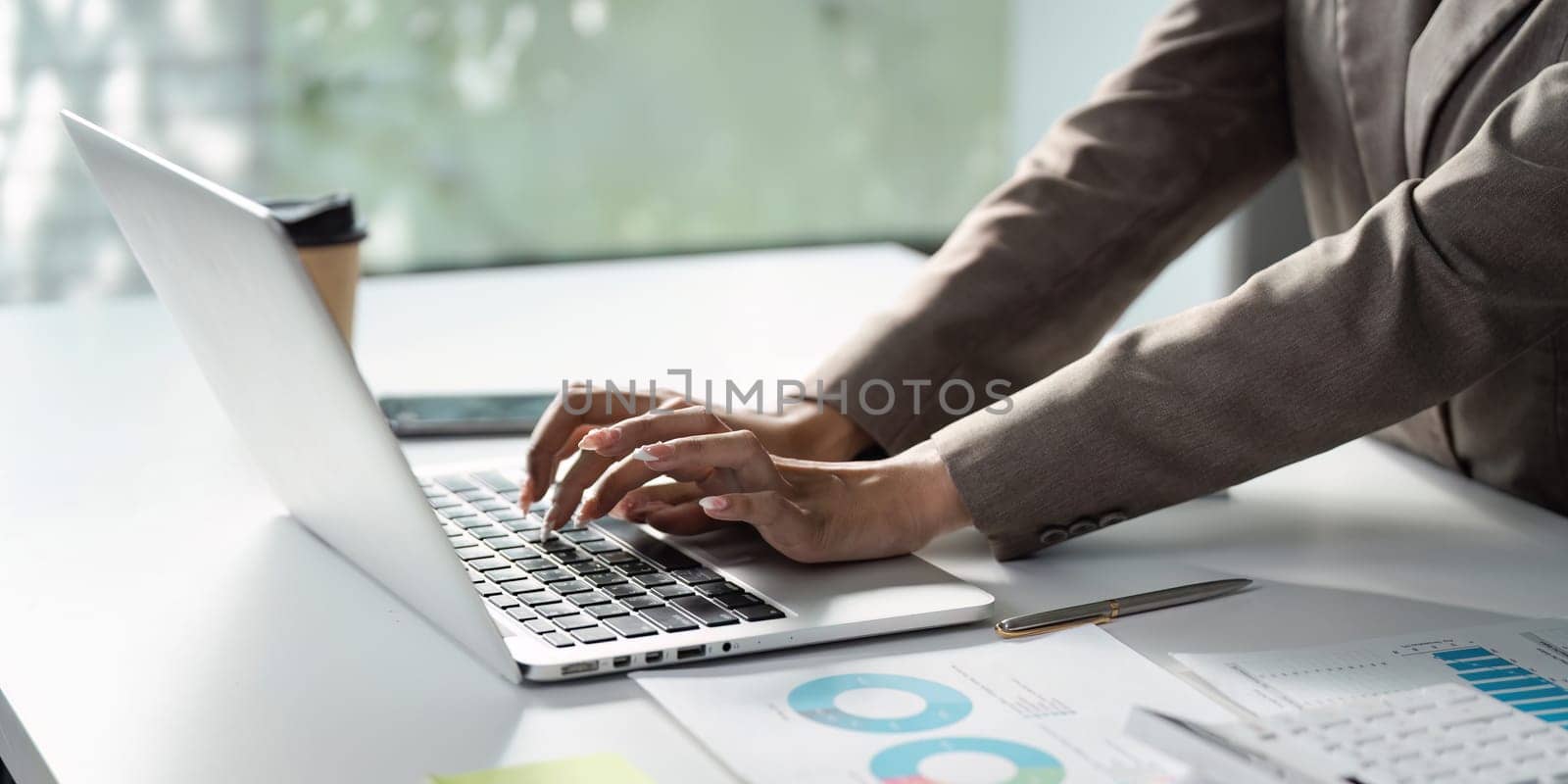A focused business professional of Asian descent types on a laptop, reviewing financial charts and reports, highlighting productivity and analysis in the workplace.