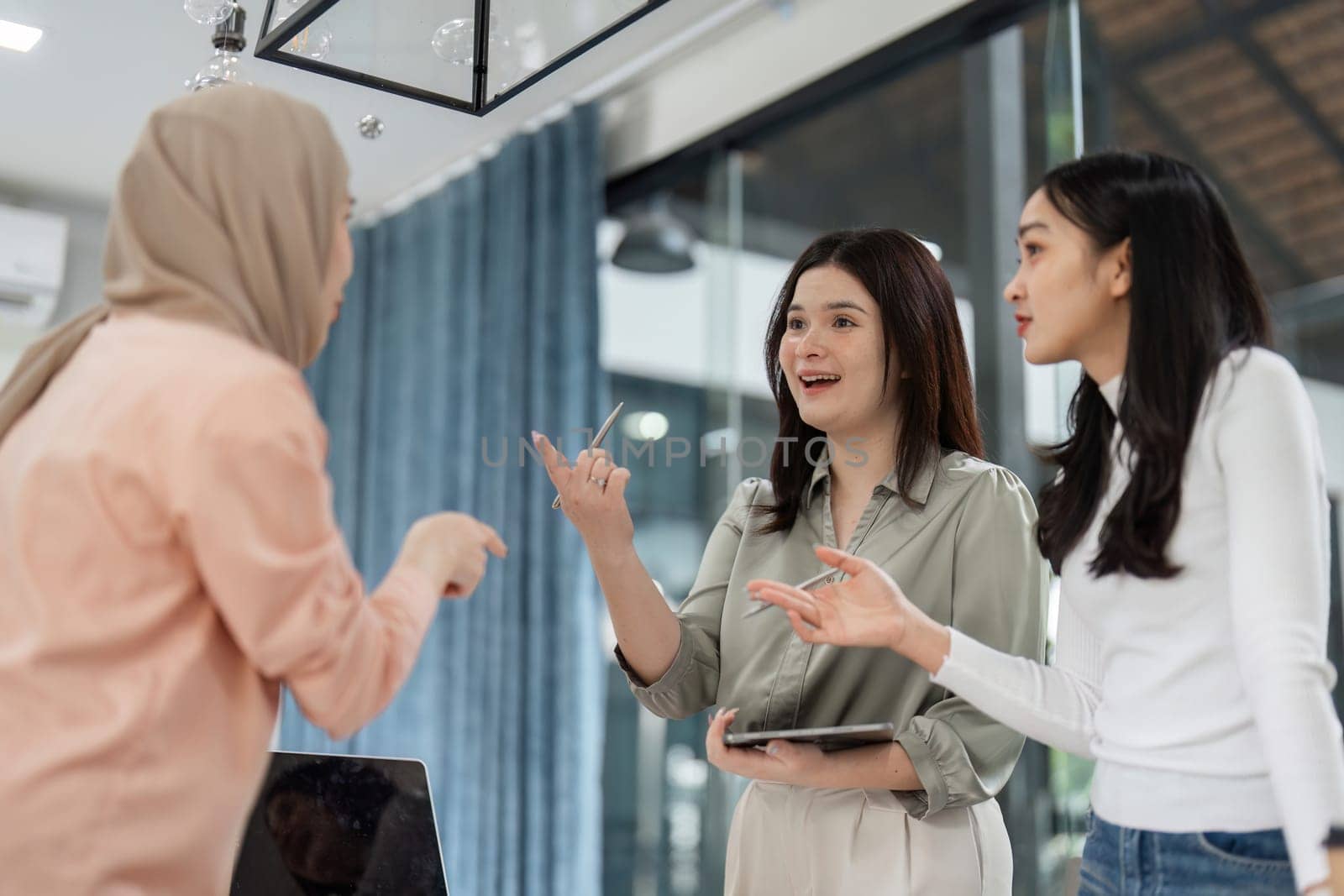 Three diverse women engage in a lively discussion in a contemporary office setting, sharing insights and ideas.