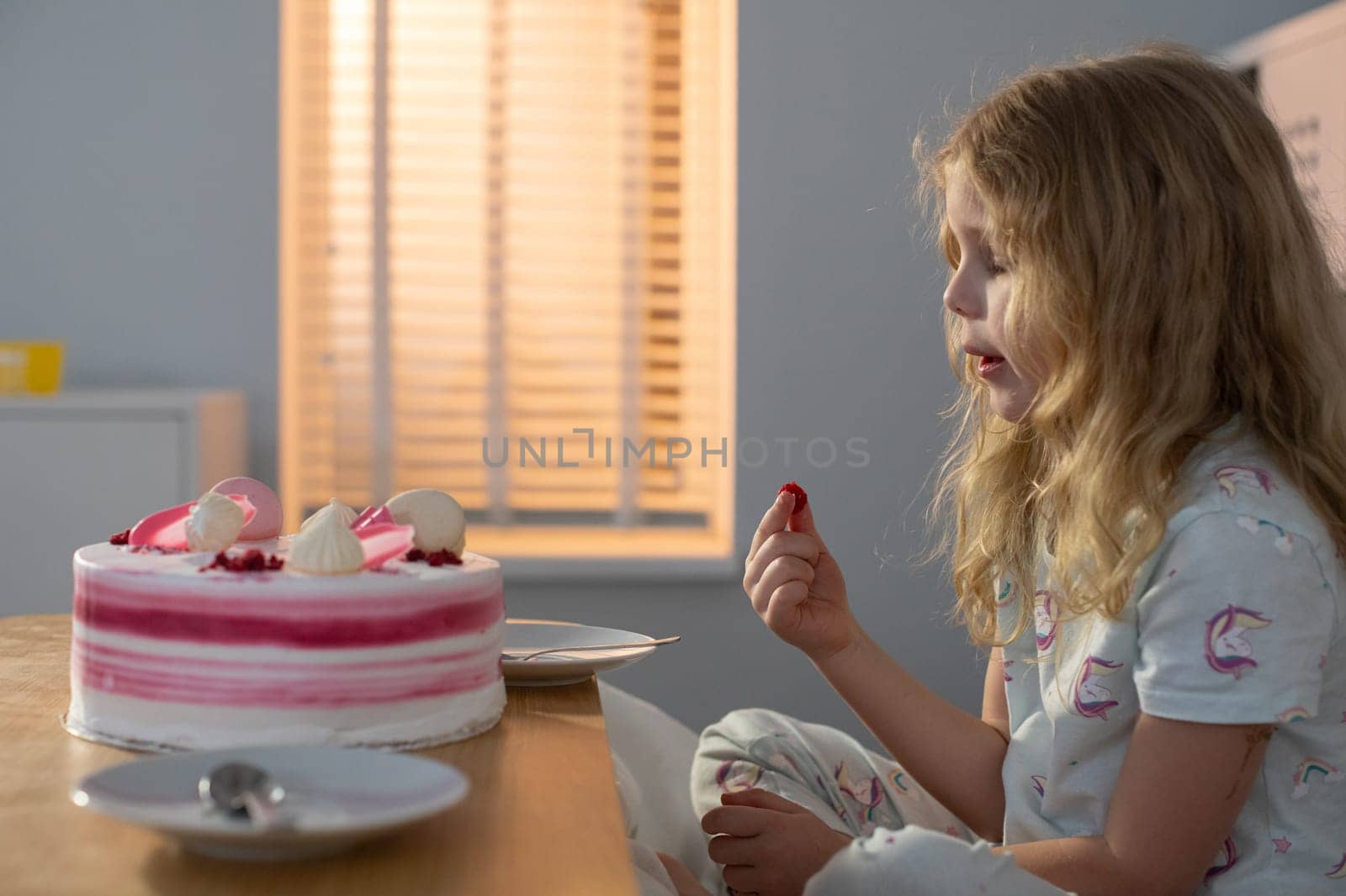 A young girl happily savors a delightful piece of cake in a cozy, softly lit room, creating a joyful moment