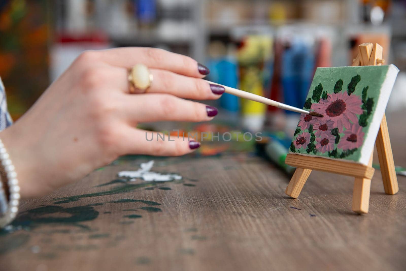 A skilled hand delicately paints beautiful flowers on a small canvas using vibrant and rich colors to create art