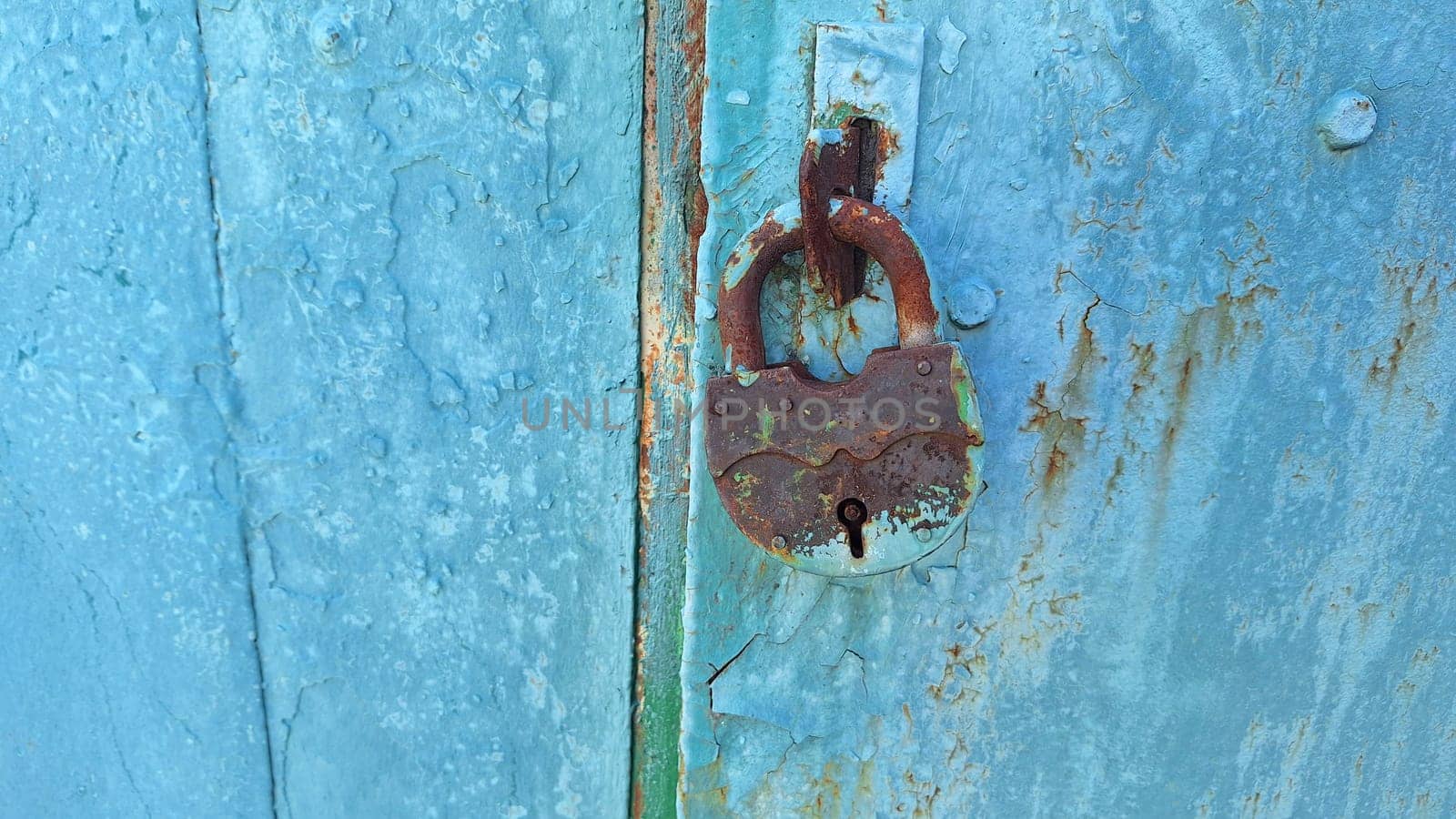 Rusty lock on weathered blue door: urban decay and vintage charm.