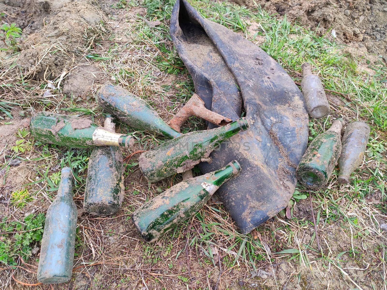 On the ground is a pile of old glass green dirty bottles and a tire tube. People throw garbage and bury garbage in the forest.