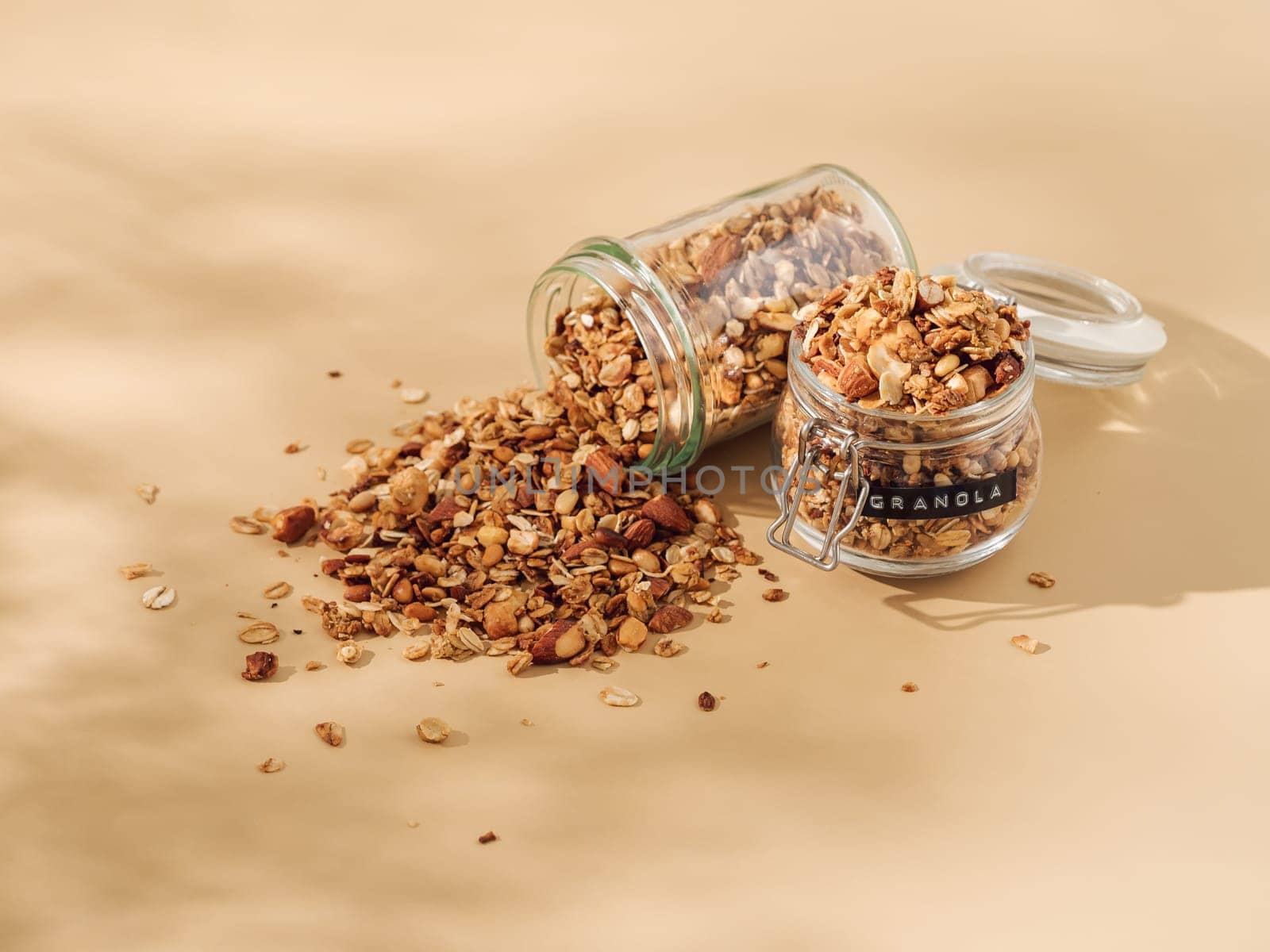 Homemade granola sprinkled of glass jar over pastel beige background. View from above. Aesthetic oat granola, beautiful shadows, champagne yellow background. Healthy breakfast concept. Copy space