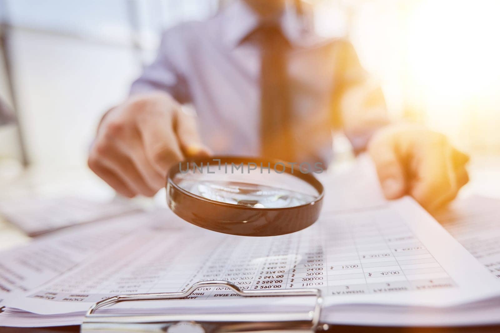 man looking through a magnifying glass to documents notebook.