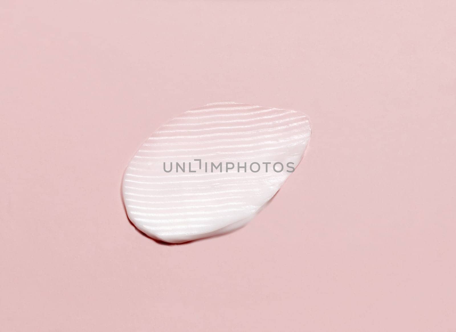Cosmetic cream smear on a light pink top view. Skincare product texture - cream or nourishing balm. Moisturizing face cream or body lotion swipe smudge. Daily personal care