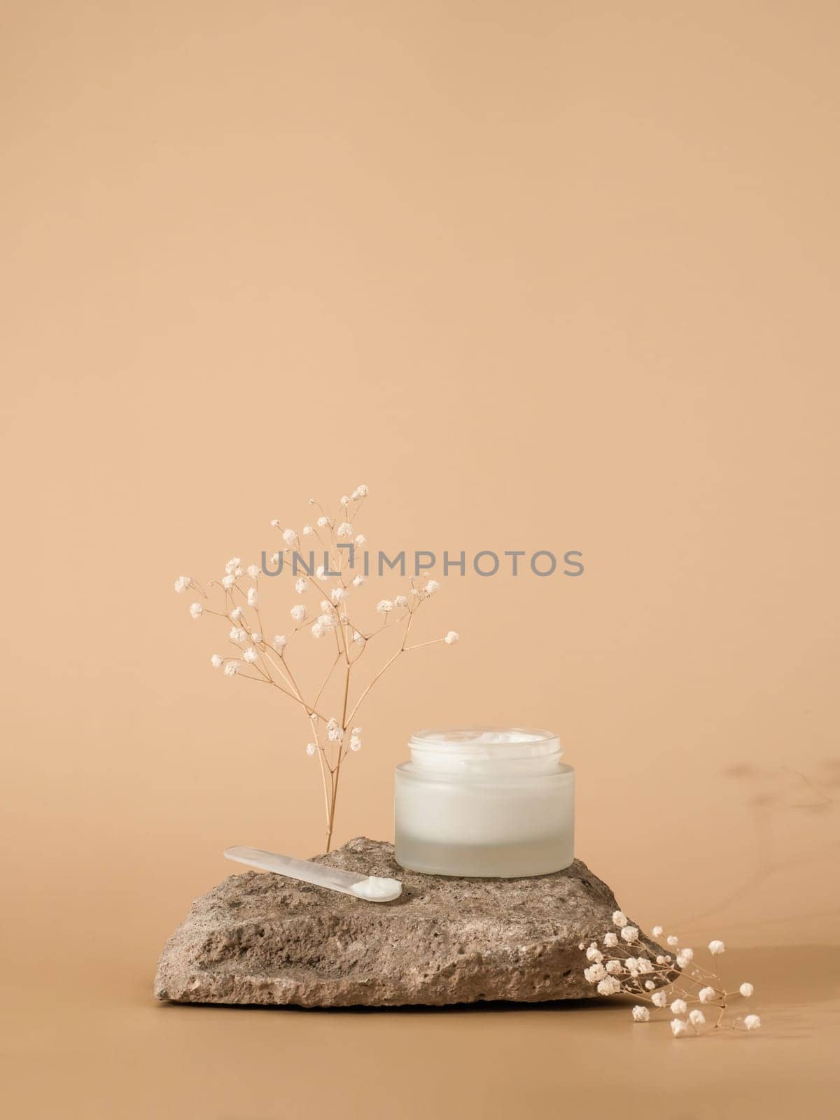 Cosmetic cream or moustirizer on stone over pastel beige background. Open round glass jar face cream and spatula. Copy space. Vertical. Mockup