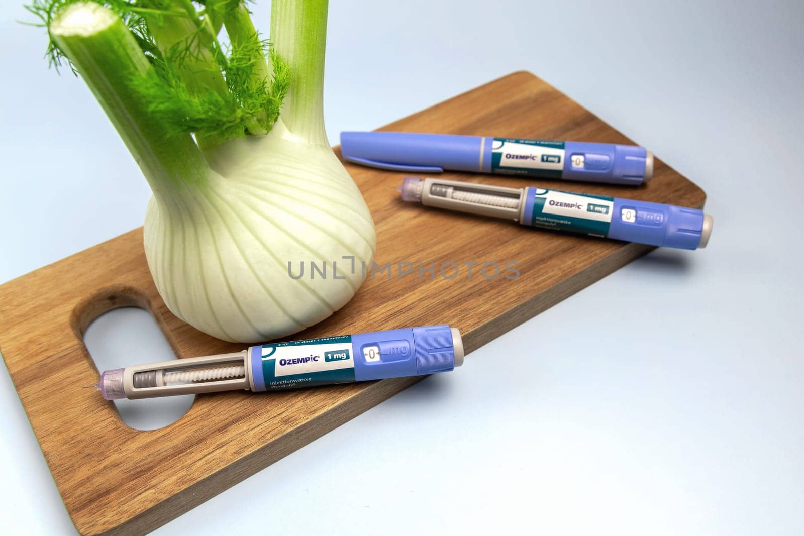 Hands holding Insulin injection pen and fennel vegetable root for diabetics and weight loss. Copenhagen, Denmark - February 16, 2025