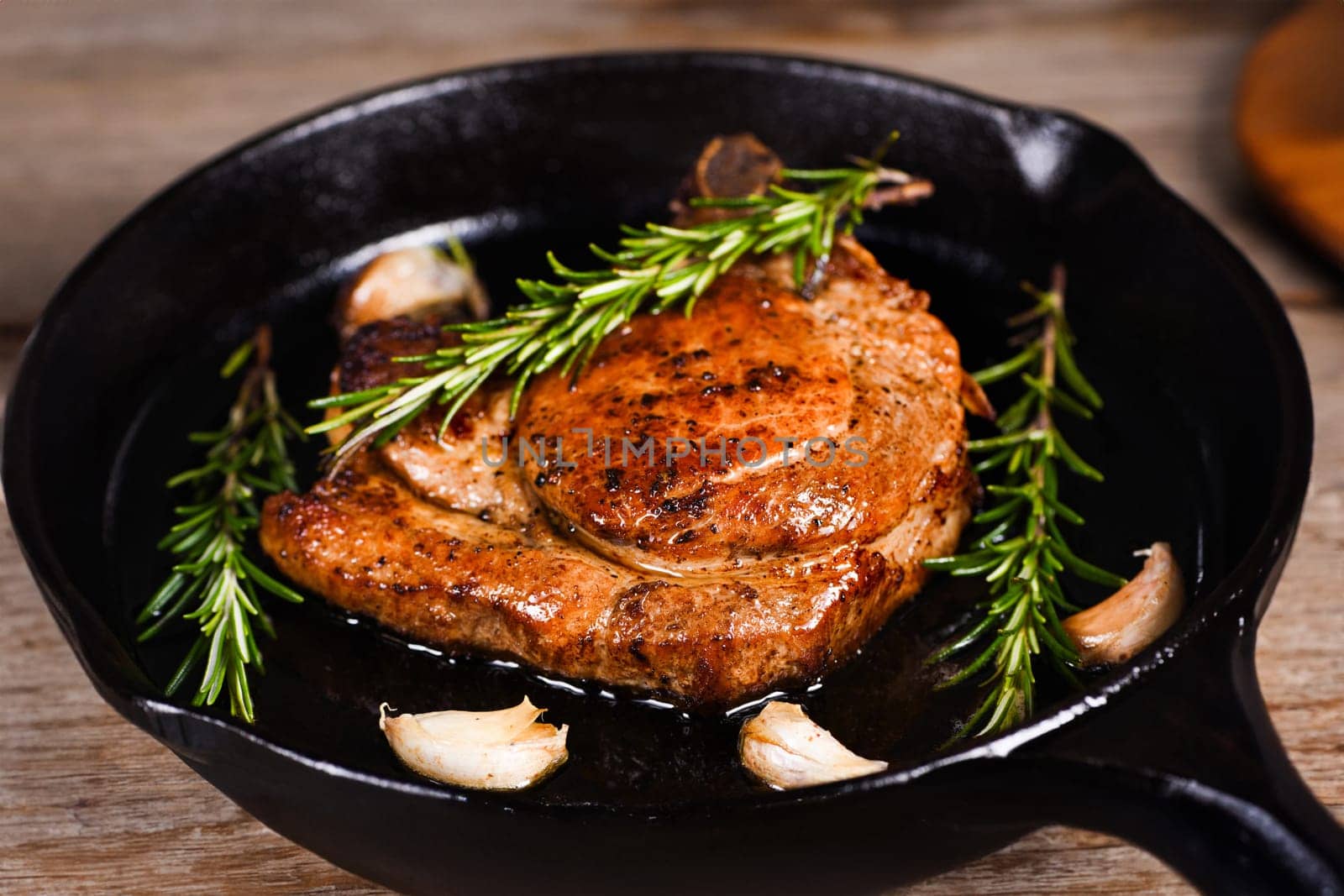 Pork cutlet on the bone in a piece of butter with garlic and rosemary in a frying pan 