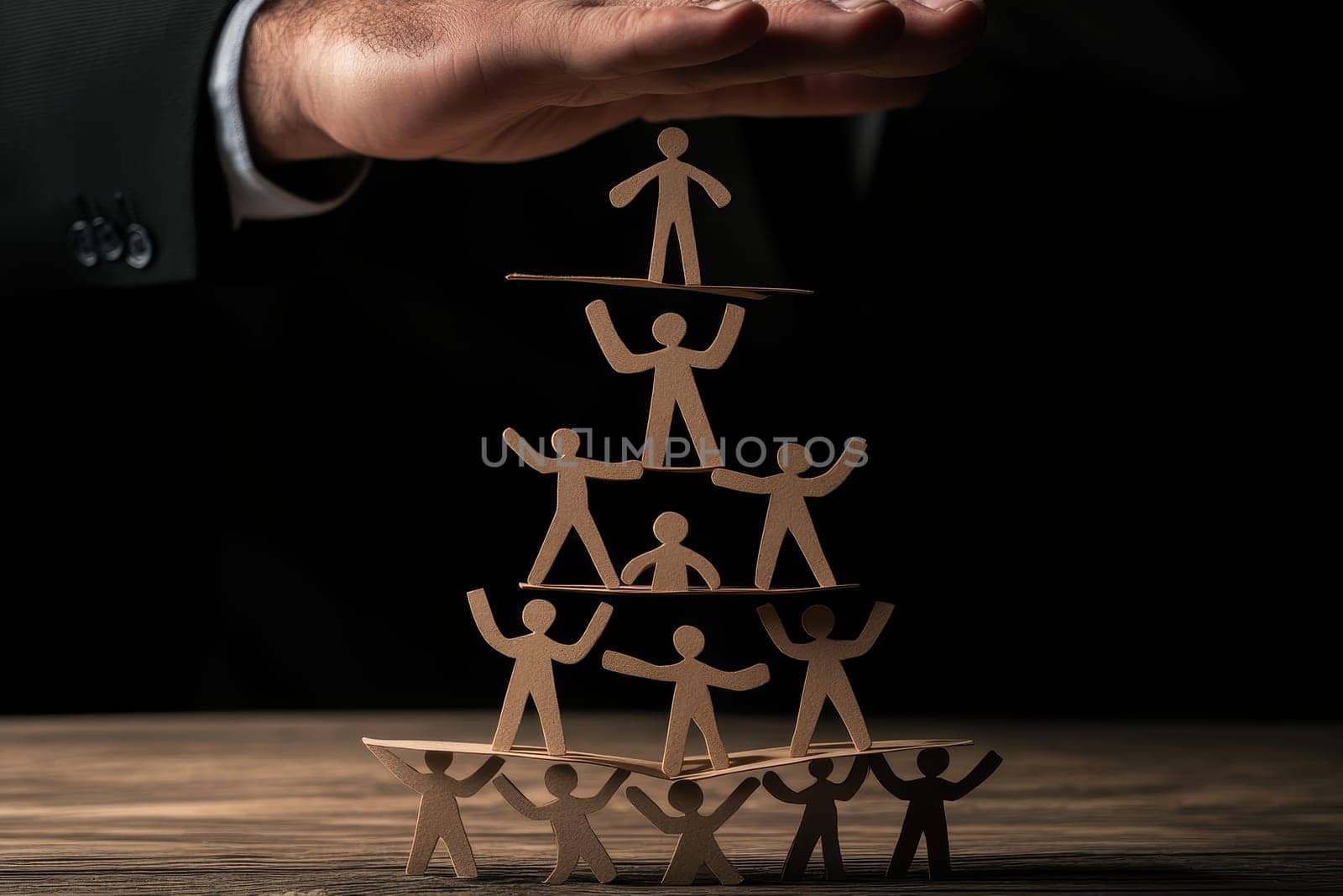 A hand lifts paper cutout figures stacked in a pyramid formation, symbolizing teamwork, support, and creativity in a business or community setting.