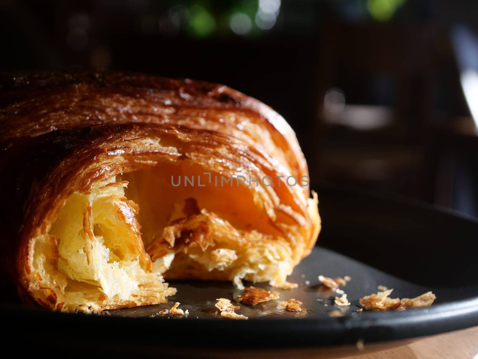 Flaky layers of a croissant are highlighted on a dark plate.