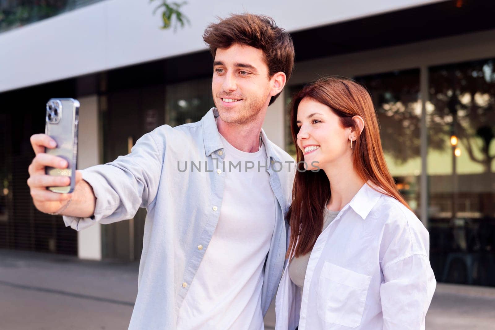 man and a woman are taking a selfie together, the man is holding a cell phone and the woman is smiling, concept of technology and urban lifestyle