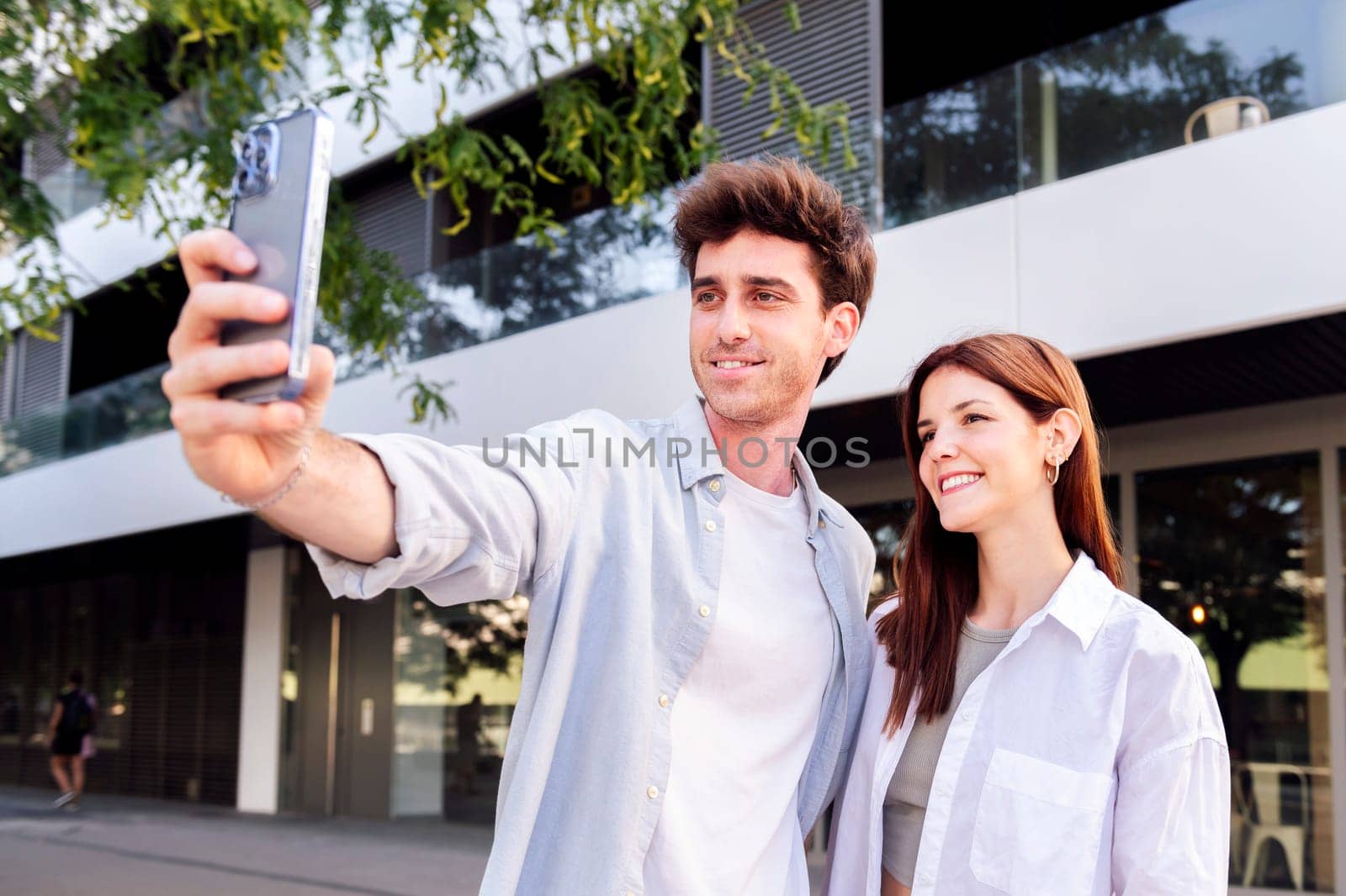 man and a woman are taking a selfie together, the man is holding a cell phone and the woman is smiling, concept of technology and urban lifestyle