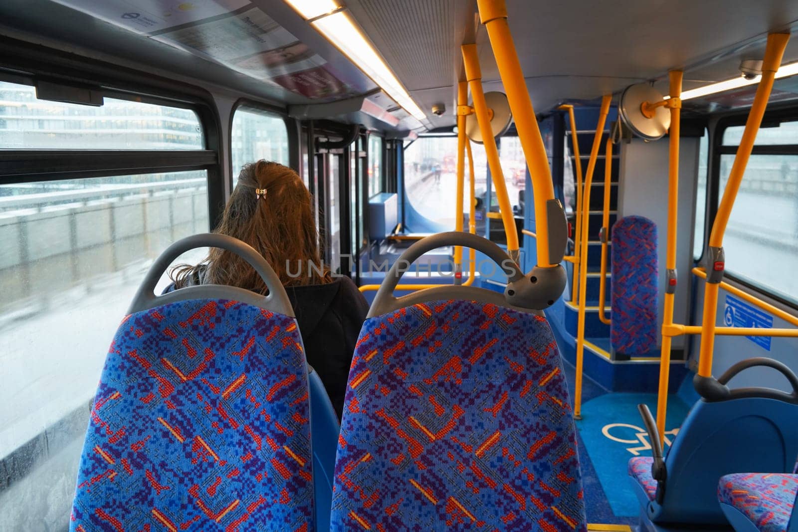 London, United Kingdom - February 01, 2019: Anonymous young female passenger travelling in otherwise empty public transport bus, view from behind, unoccupied seats visible