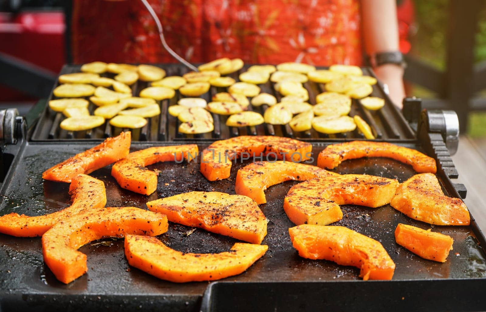 Bright orange butternut squash pieces seasoned with spices grilled on electric grill, blurred potato chips prepared in background