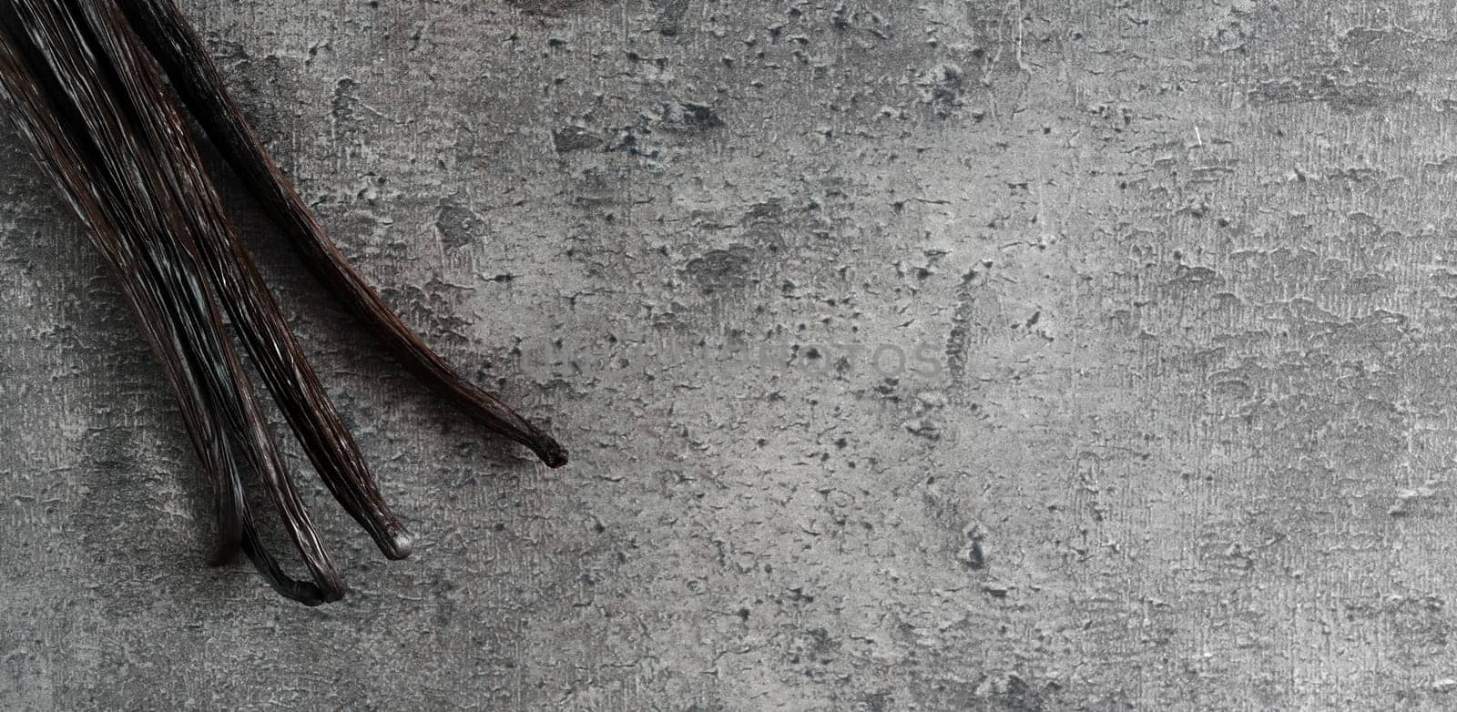 Four bourbon vanilla beans on dark stone like board, view from above, wide banner photo space for text right side