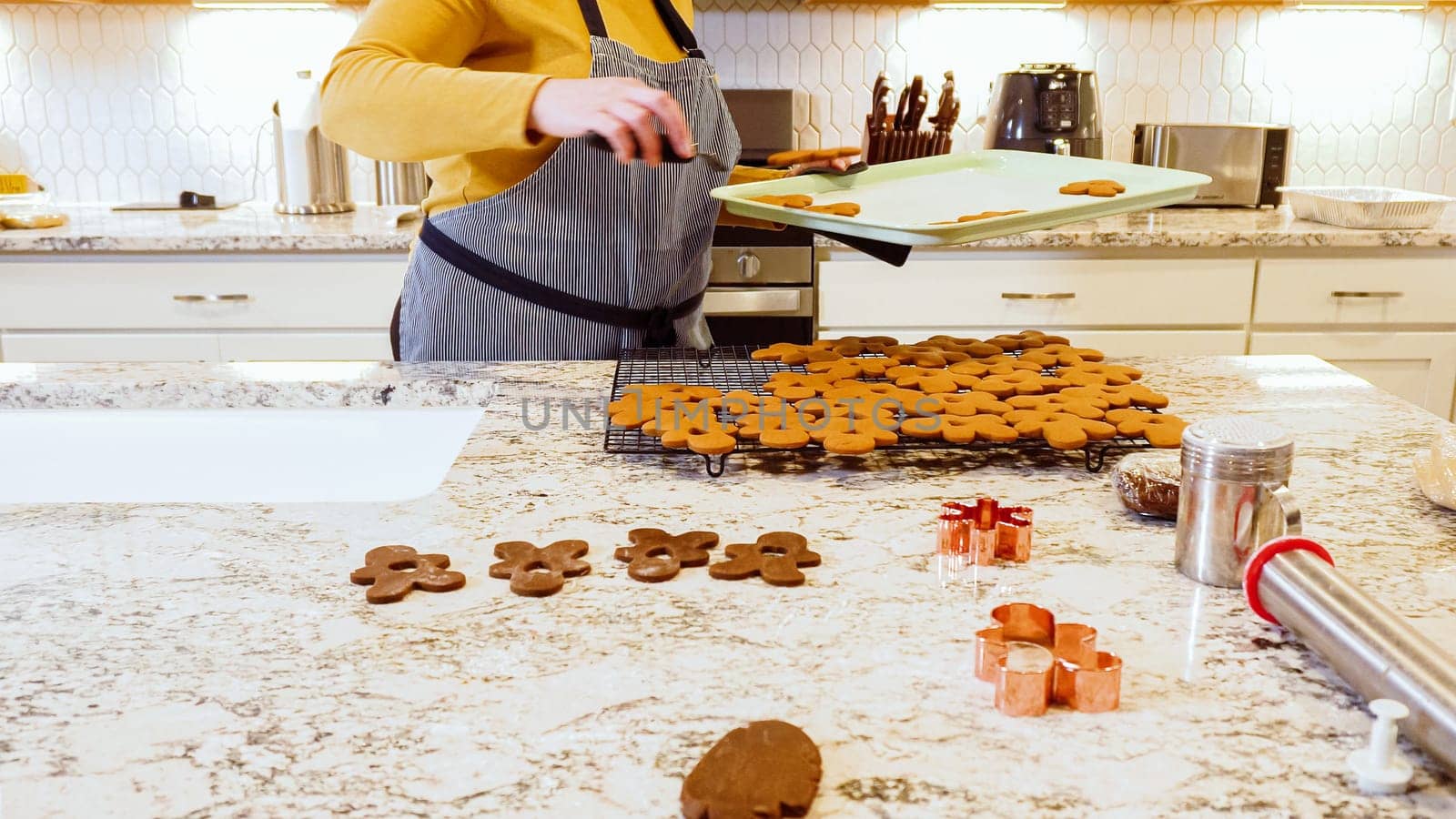 After baking to perfection, these delightful gingerbread cookies are now cooling gracefully on a wire rack, filling the modern kitchen with a warm and inviting aroma.
