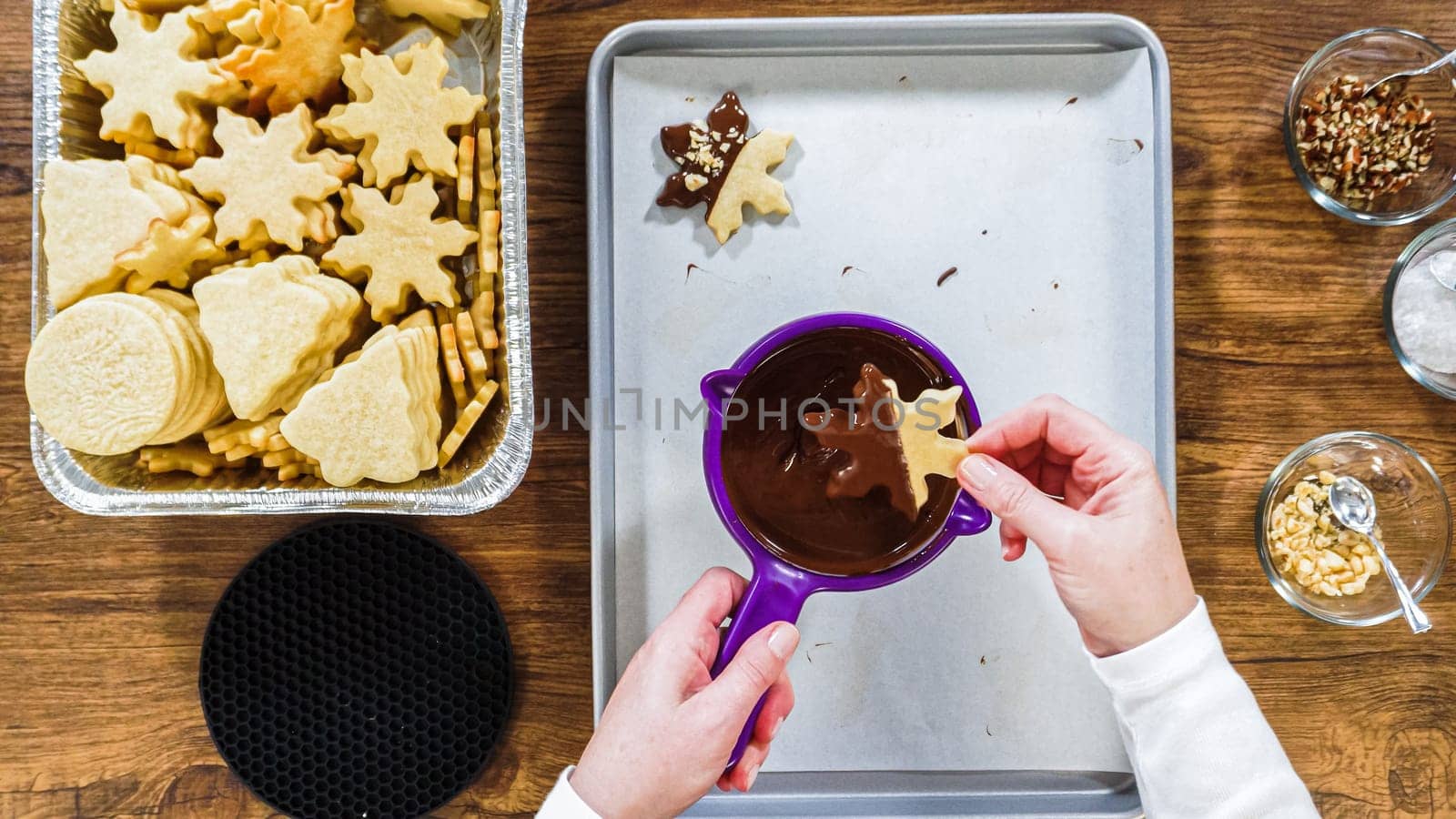 Flat lay. Creating snowflake-shaped cutout sugar cookies, dipped in chocolate, and adorned with different toppings.
