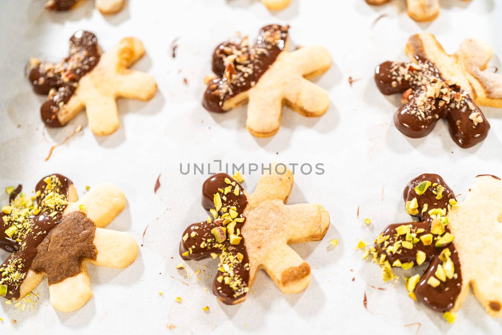 Crafting star-shaped holiday cookies dipped in chocolate and sprinkled with crushed pistachios, arranged on parchment paper.