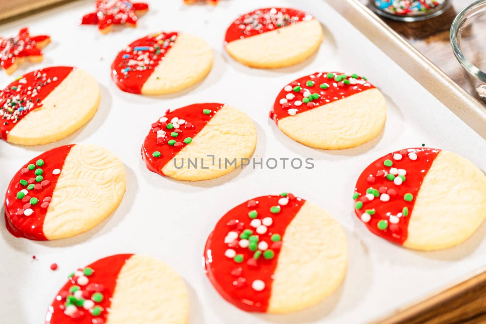 Skillfully decorating cookies with vibrant red melted chocolate and a generous sprinkle of vibrant green, creating a festive holiday treat.