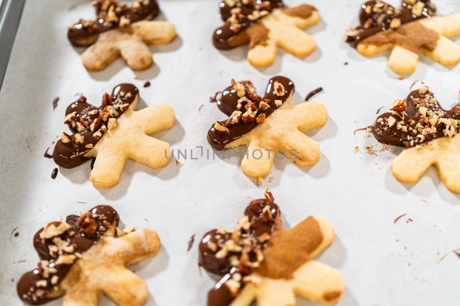 Creating snowflake-shaped cutout sugar cookies, dipped in chocolate, and adorned with crushed pecan nuts, elegantly presented on parchment.