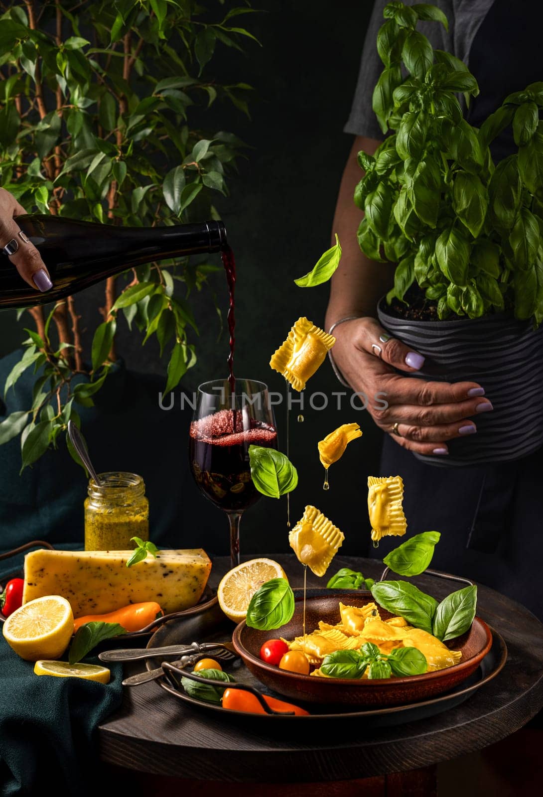 Chef pouring red wine while preparing a plate of delicious ravioli with fresh basil leaves, cheese, and vegetables