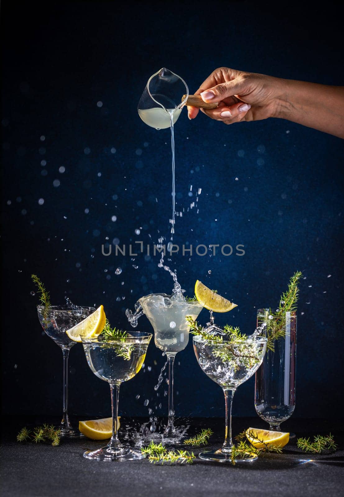 Bartender pours gin into cocktail glasses, creating a dynamic splash and highlighting the refreshing mix of lemon and juniper berries