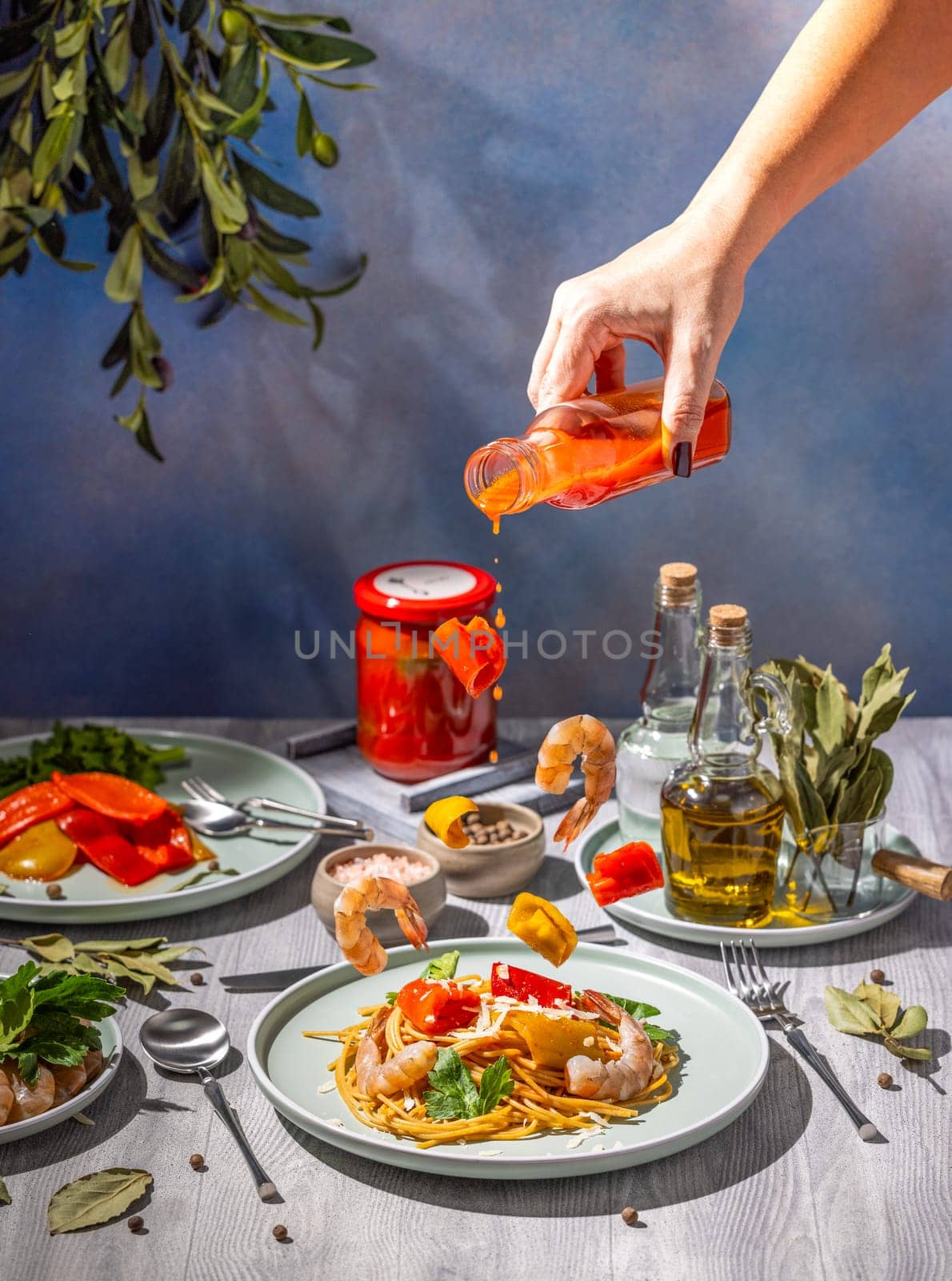 Chef's hand pouring spicy sauce from a bottle onto a delicious shrimp scampi dish with ingredients flying in mid-air, creating a dynamic culinary scene