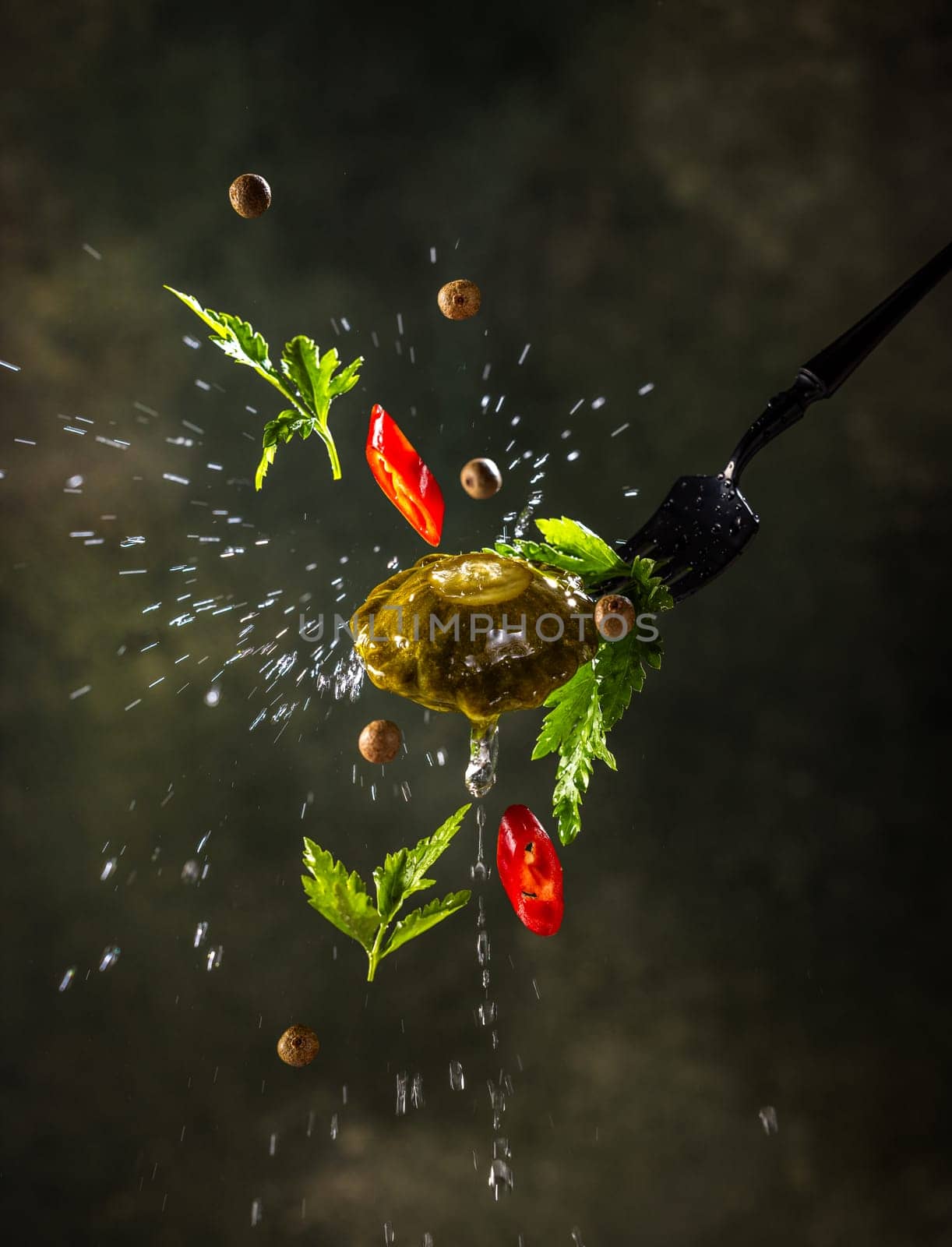 Pattypan squash, fresh herbs, red chili pepper, and spices are flying on a fork with water splashing against a dark background